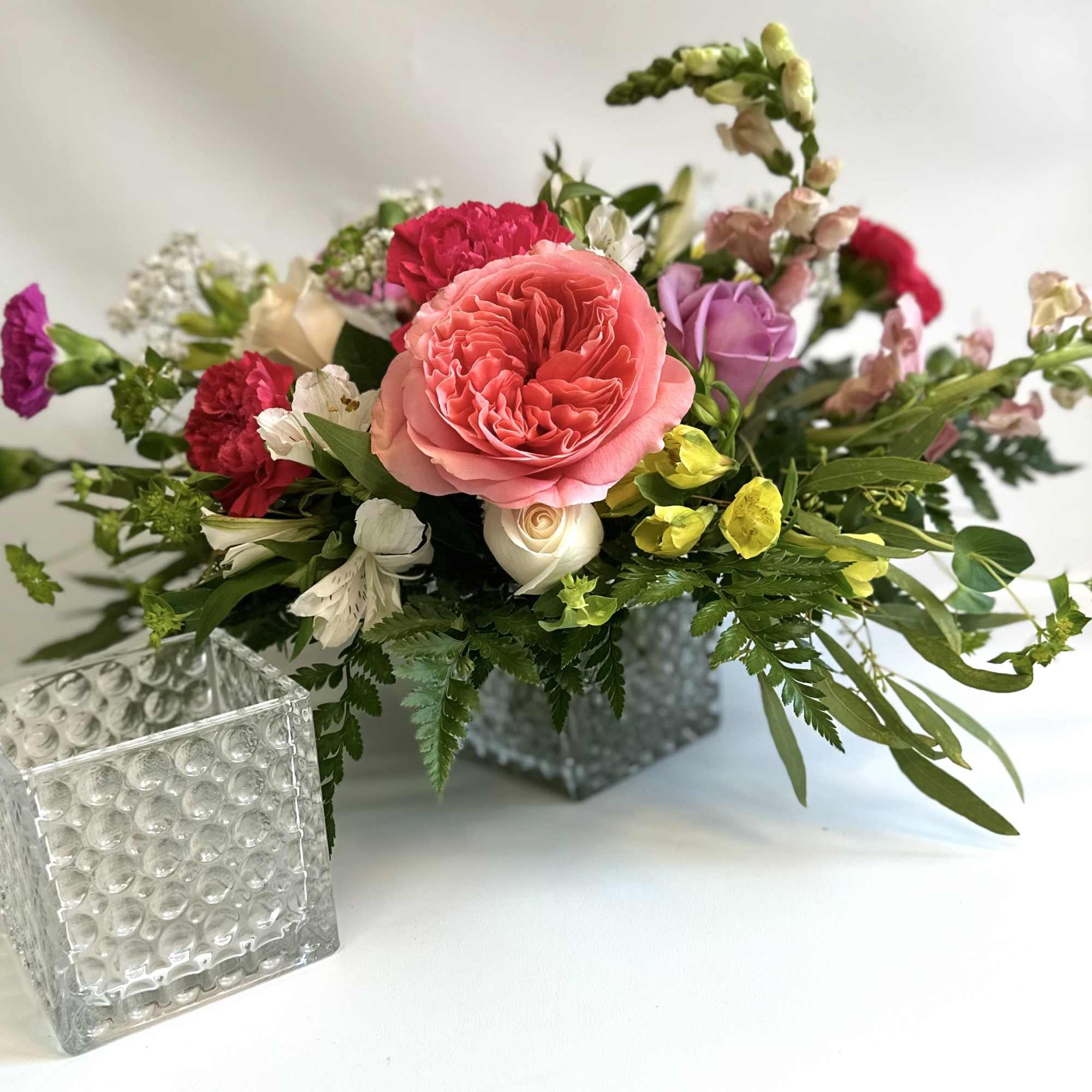 Mixed bouquet in a square glass vase with pink, red, purple, and yellow flowers