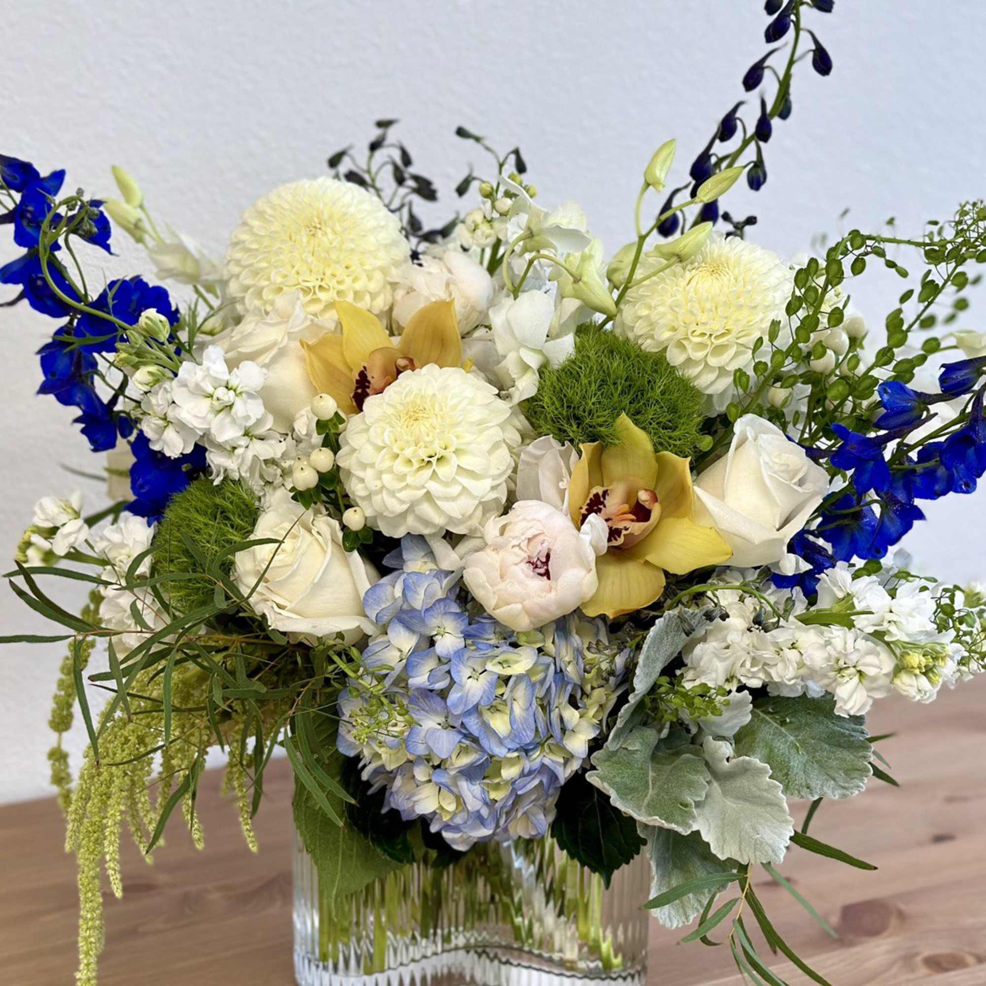 Mixed bouquet in a clear glass vase with white, blue, yellow, and pale pink flowers