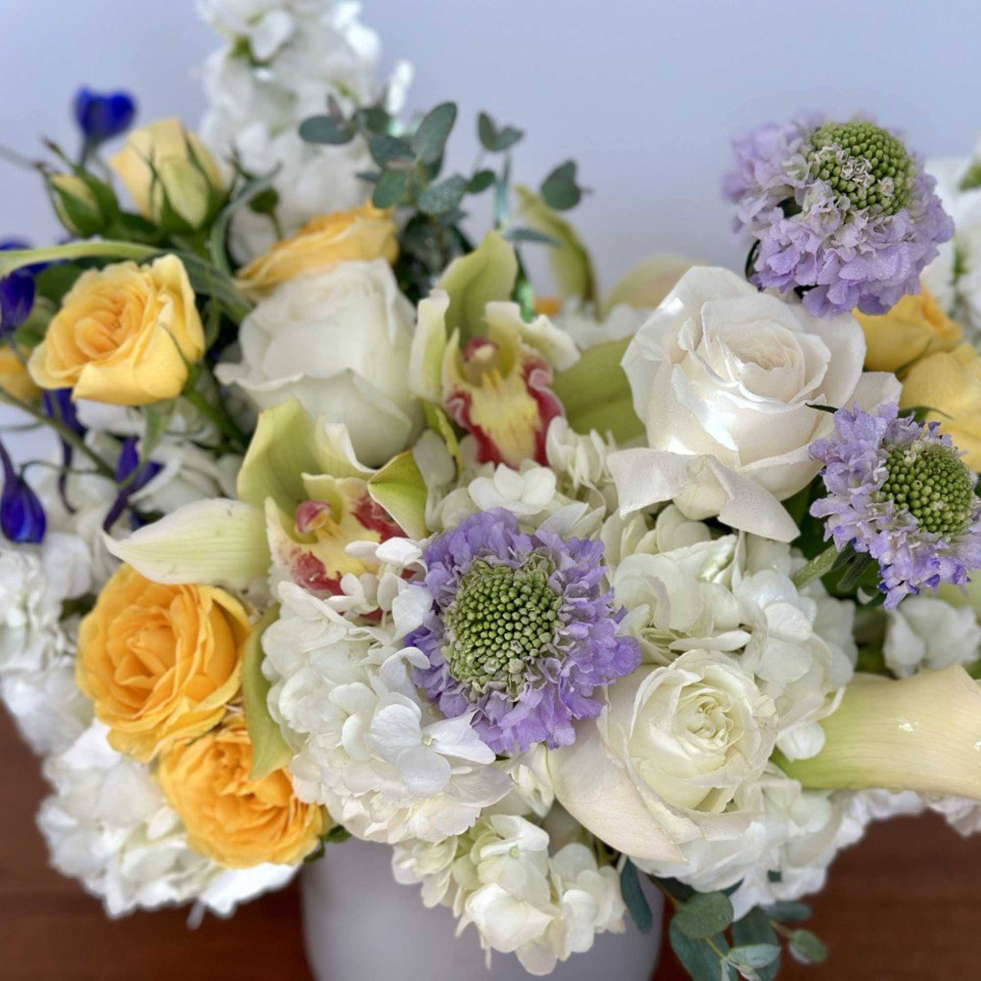 Bouquet of white and yellow roses with purple blooms in a vase
