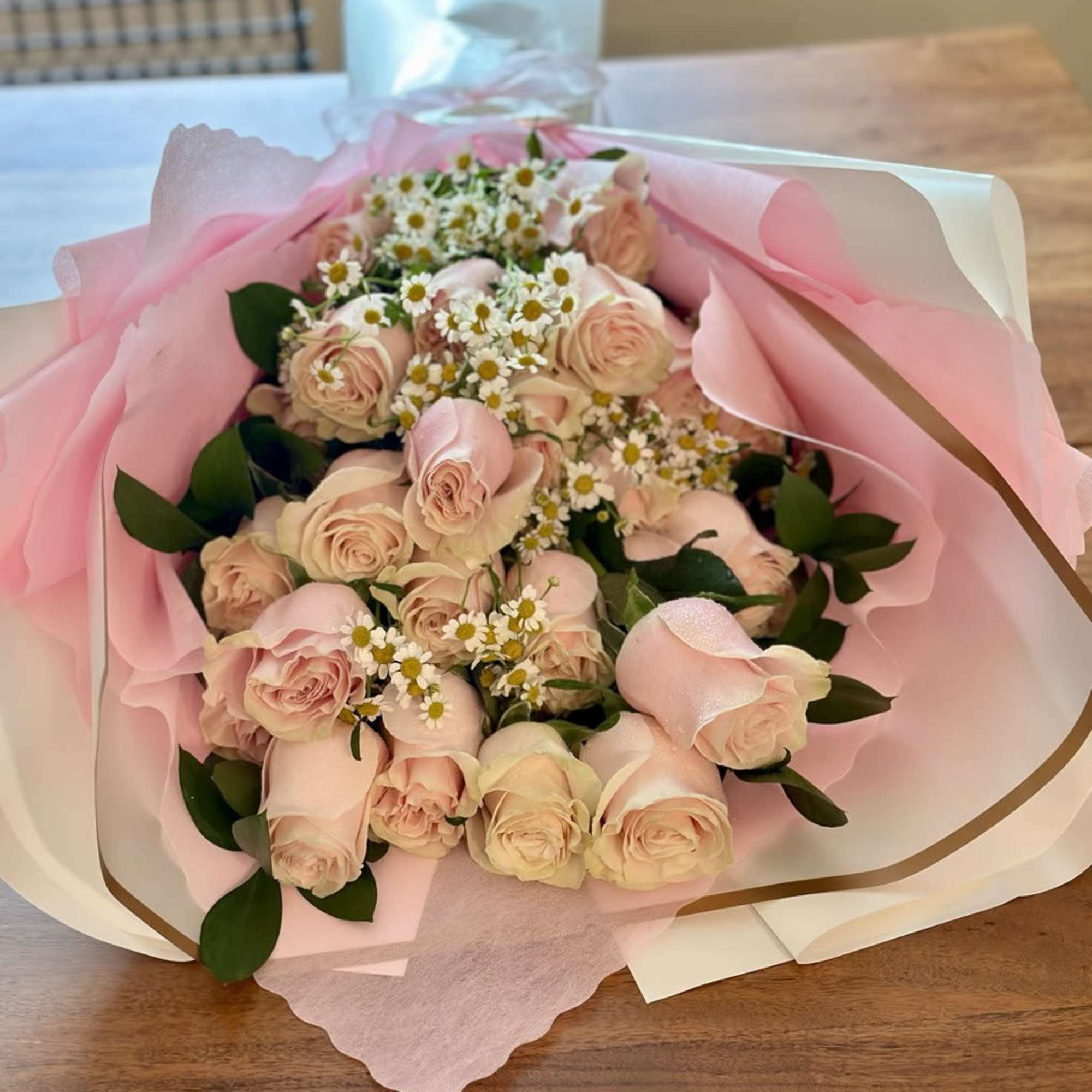 Bouquet of pale pink roses with small white daisies wrapped in pink paper