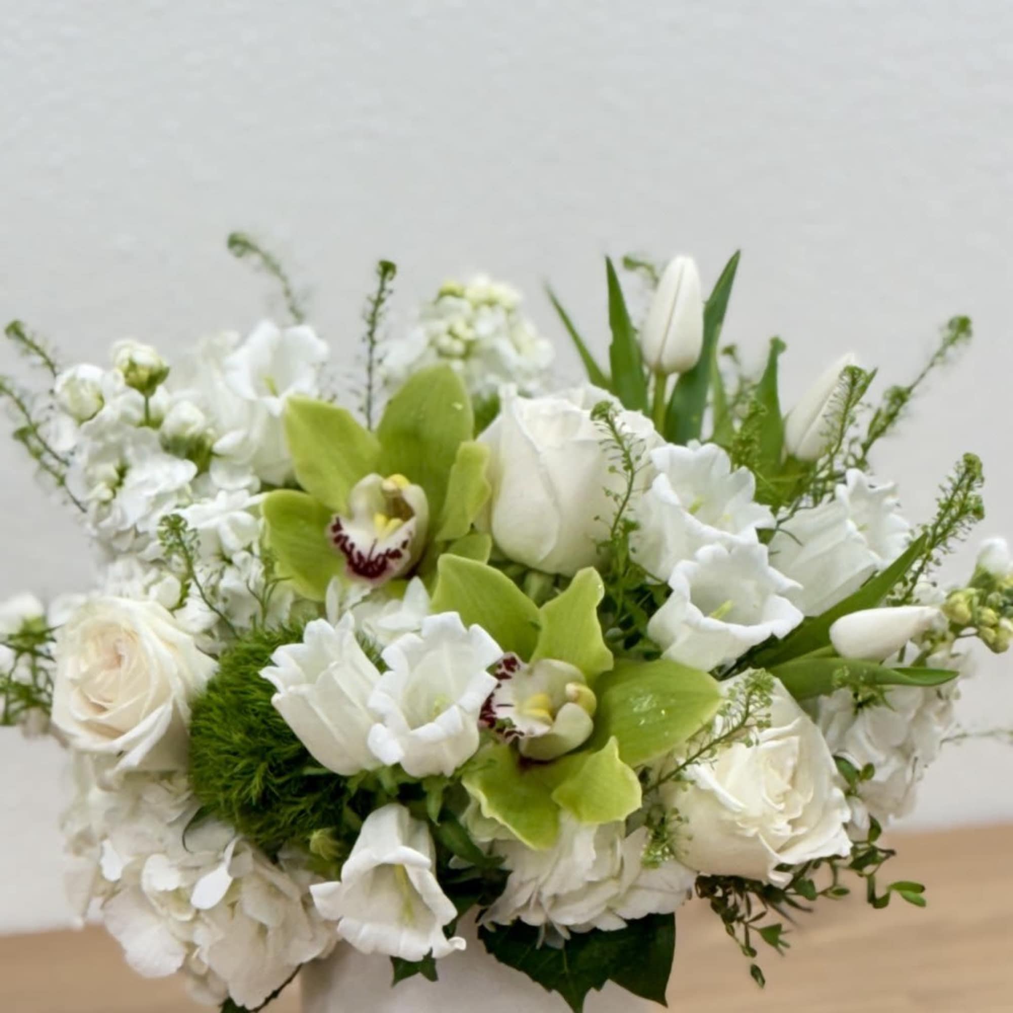 White floral arrangement with green orchids in a white vase