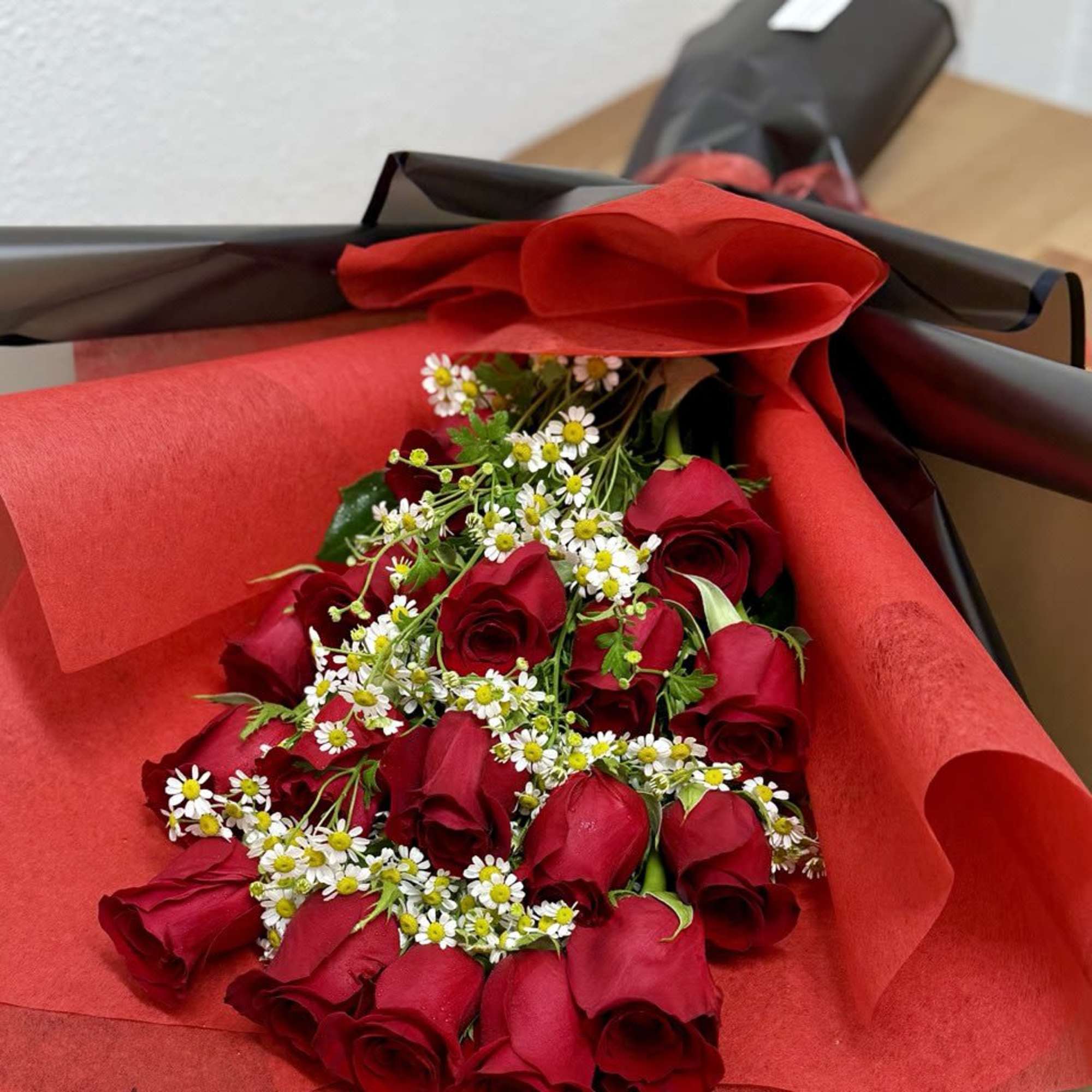Bouquet of red roses with small white daisies wrapped in red and black paper