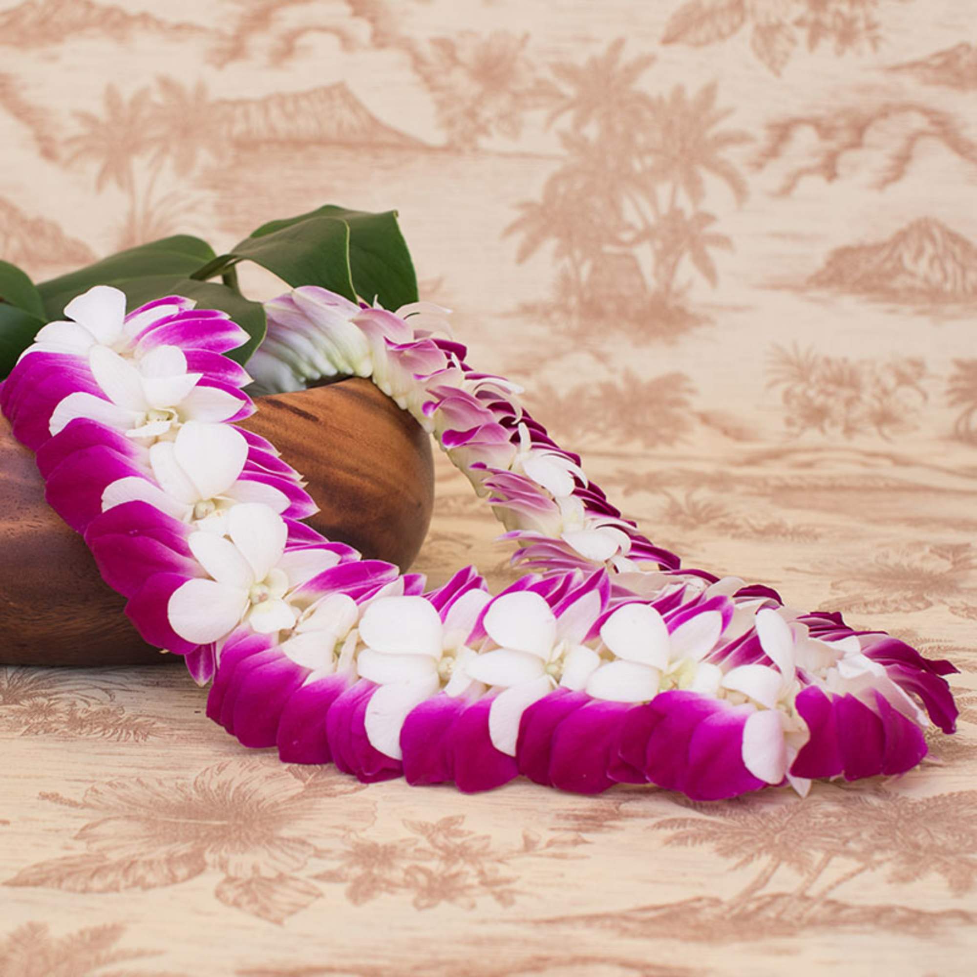 Purple and white orchid lei draped over a wooden bowl on a patterned surface
