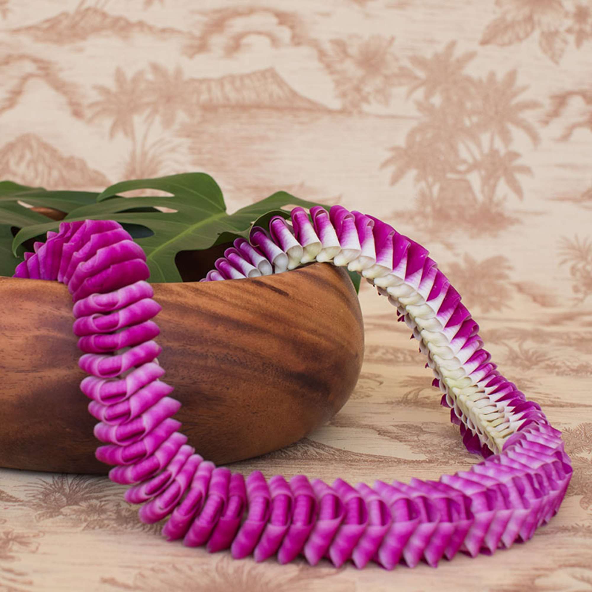 Purple and white orchid lei draped over a wooden bowl with a tropical background