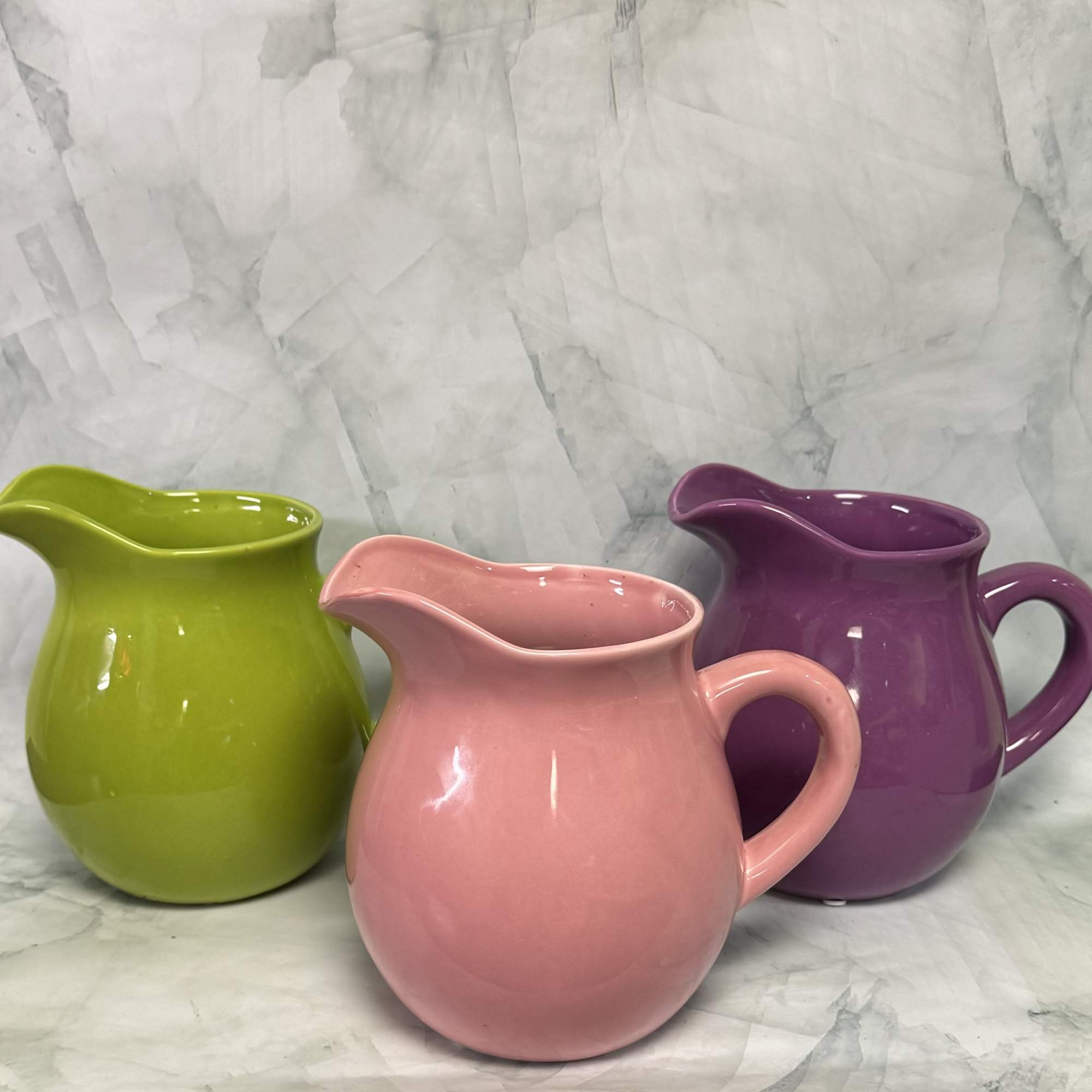 Three glossy ceramic pitchers in green, pink, and purple