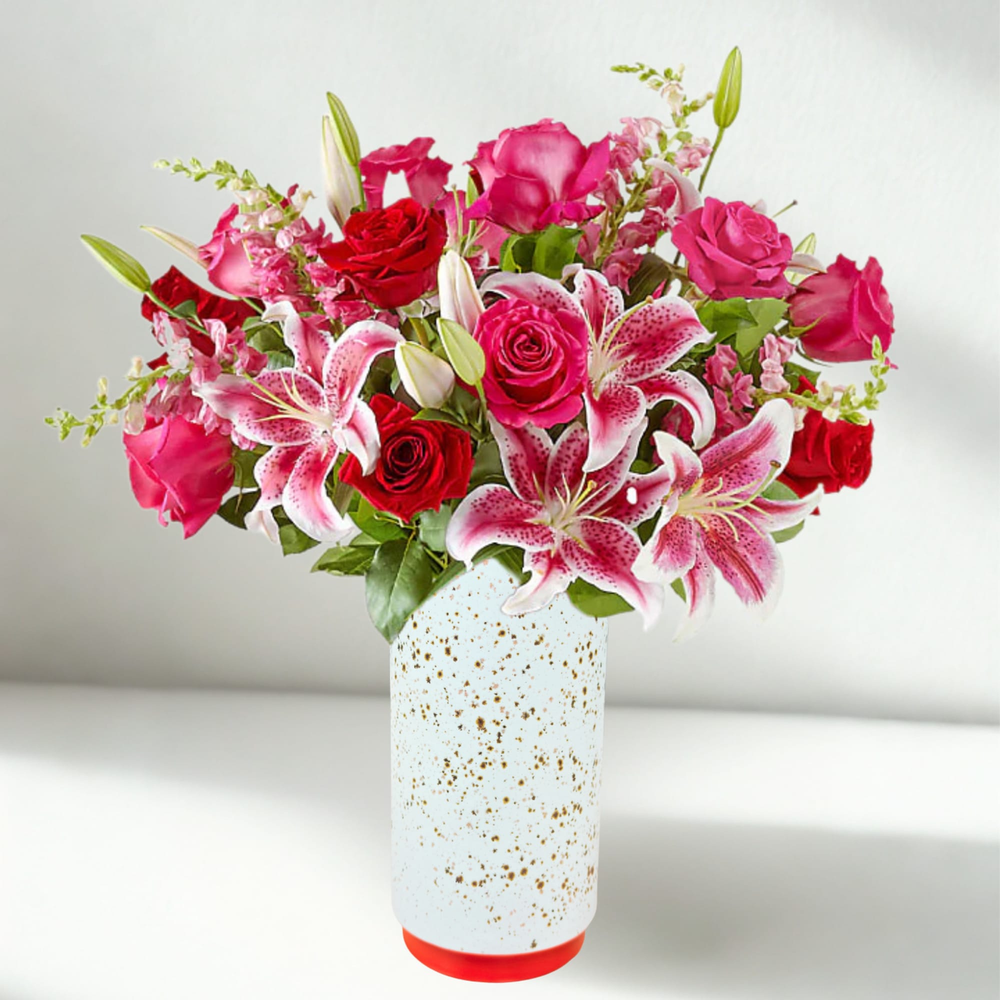 Pink and red roses with lilies in a white speckled vase