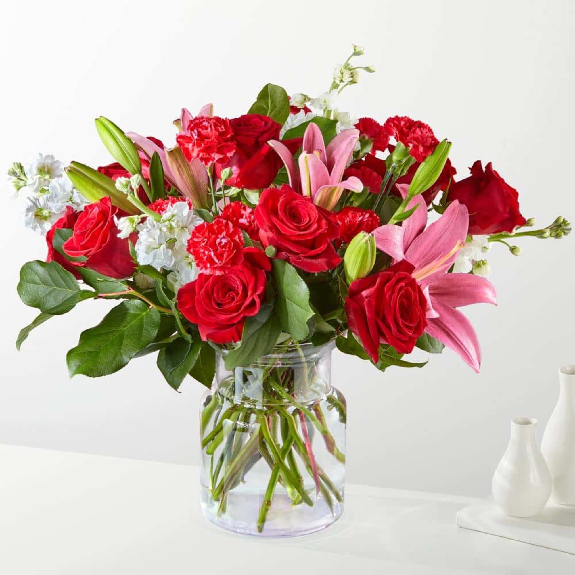 Bouquet of red roses, pink lilies, and white flowers in a glass vase