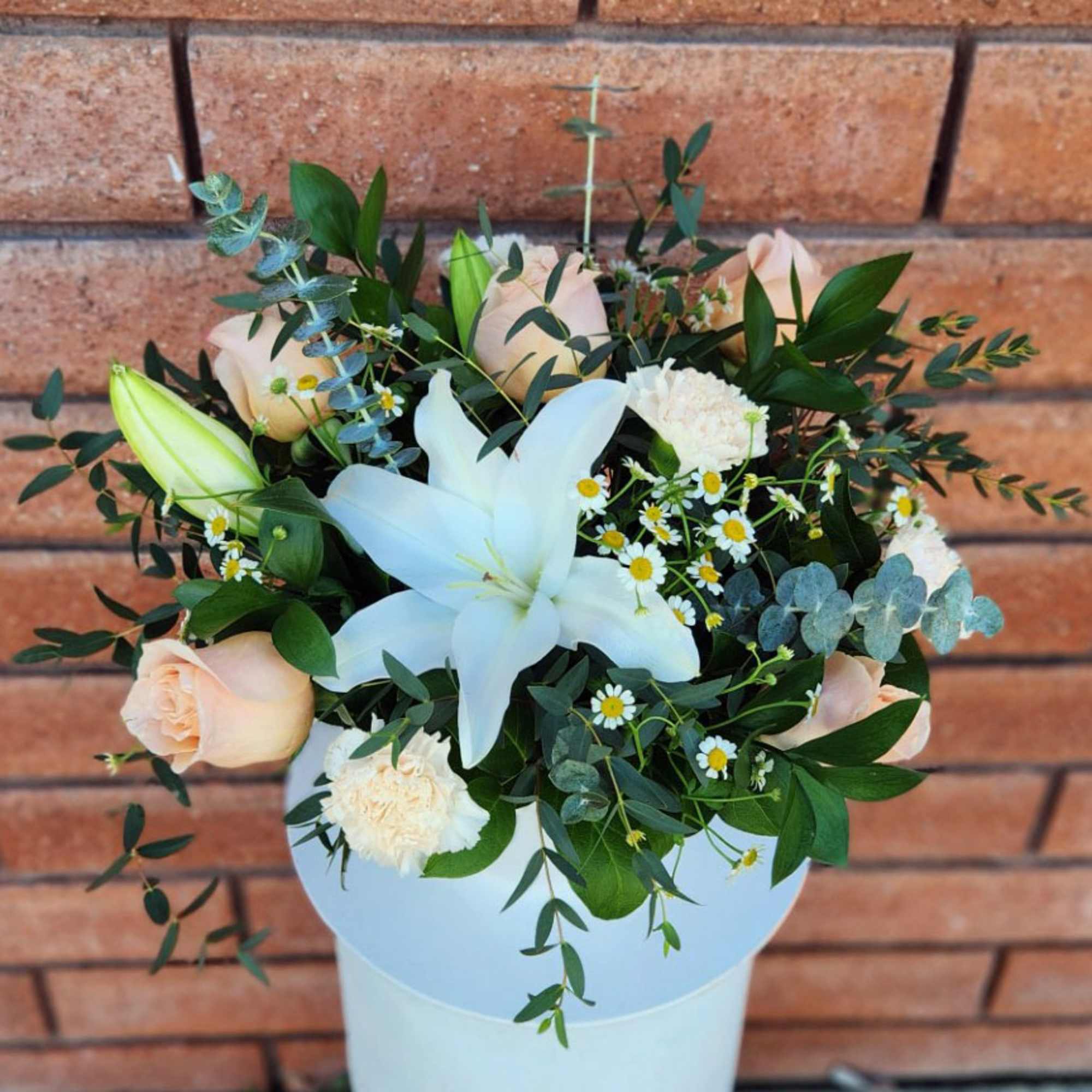 White lily with peach roses, cream carnations and small daisies in a white hatbox-style container