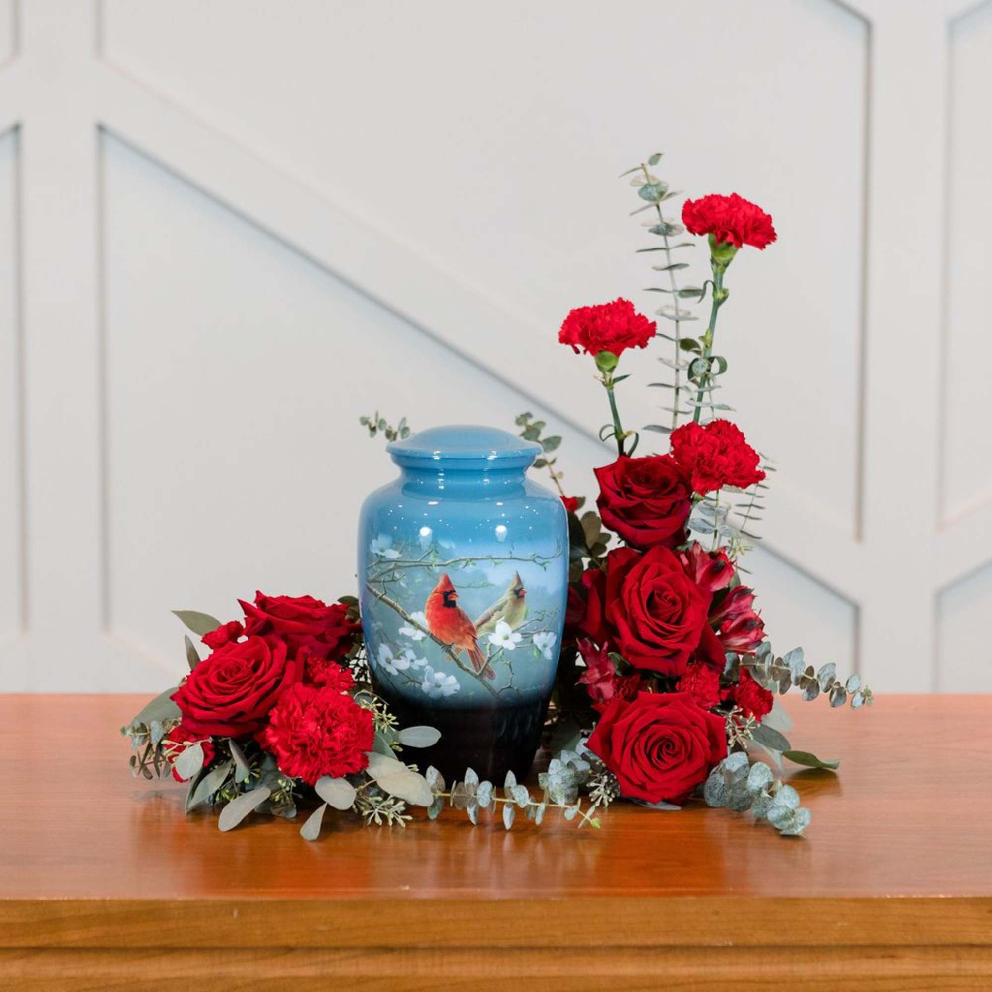 Red roses and carnations arranged around a blue urn vase