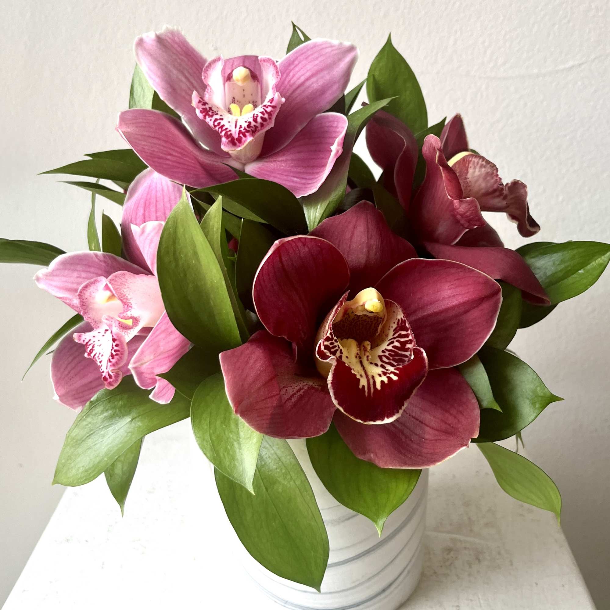 Pink and burgundy orchids arranged in a white metal pot