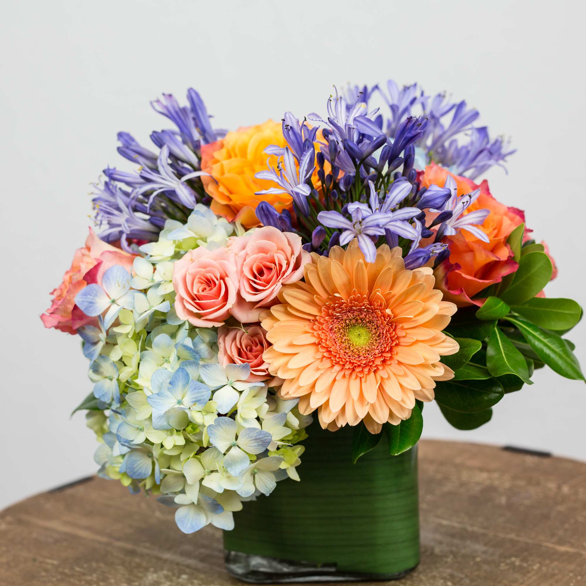 Mixed bouquet in a green vase with peach, purple, and blue flowers