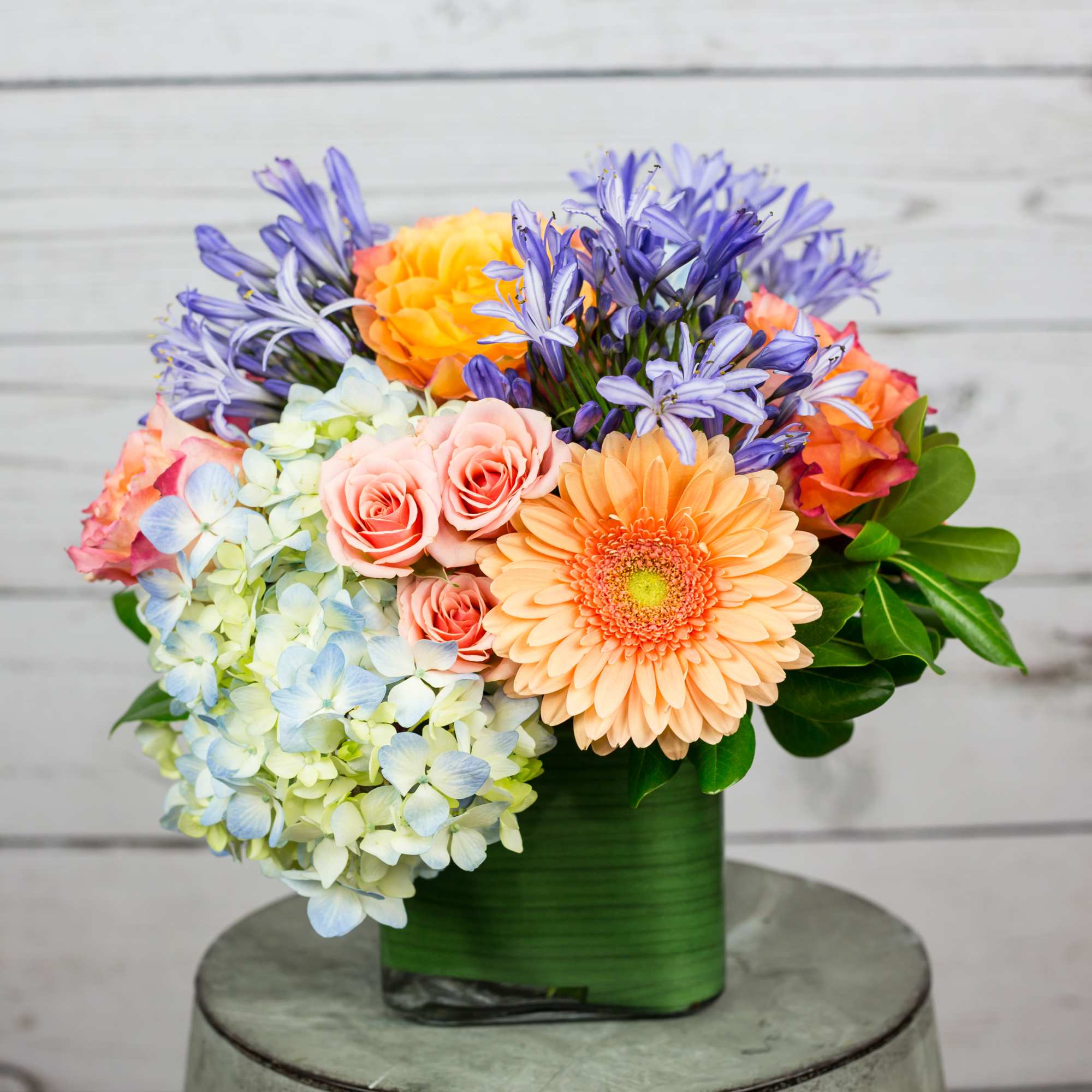 Colorful bouquet in a green wrapped container with roses, hydrangeas, and daisies