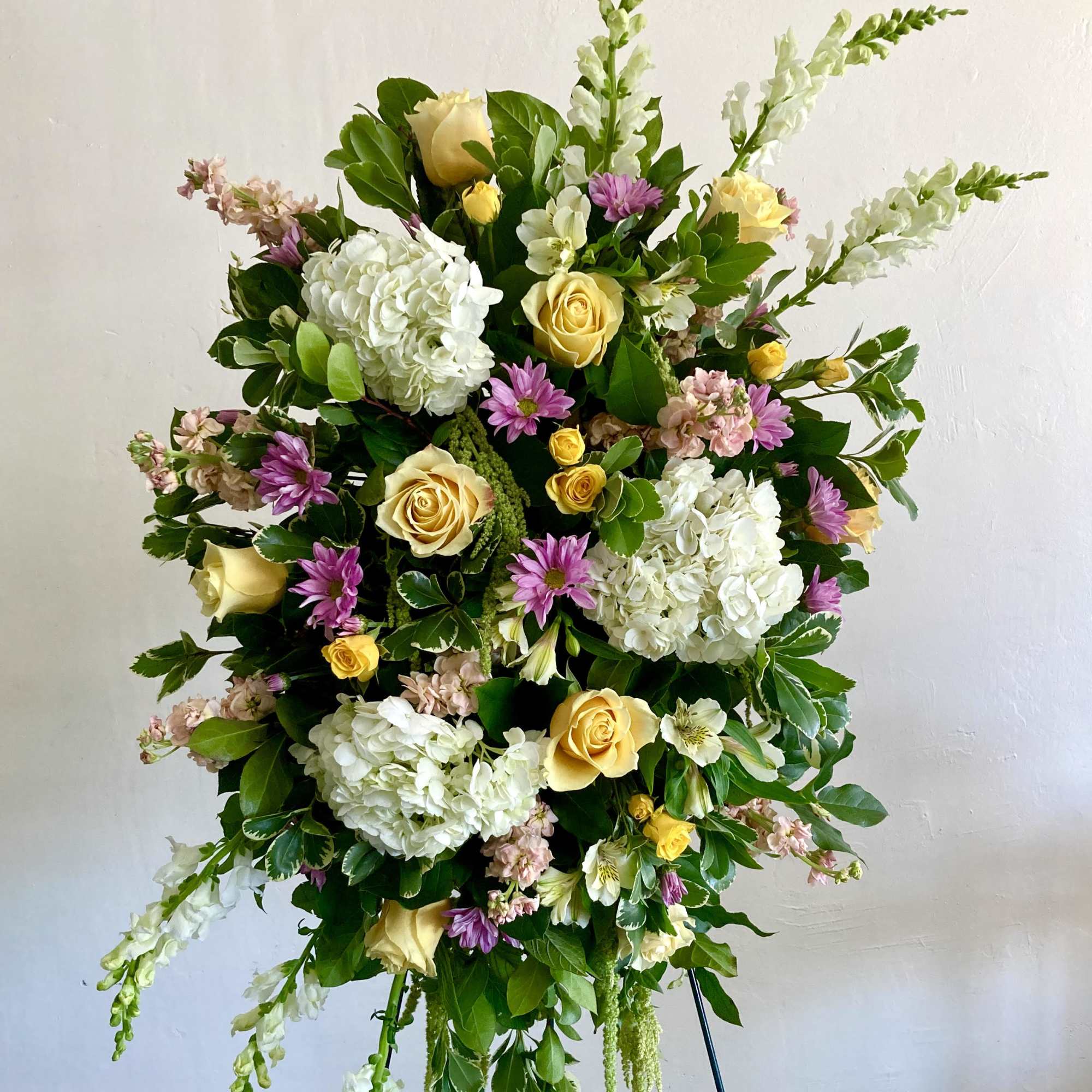 Standing floral spray with yellow roses, white hydrangeas, and purple blooms
