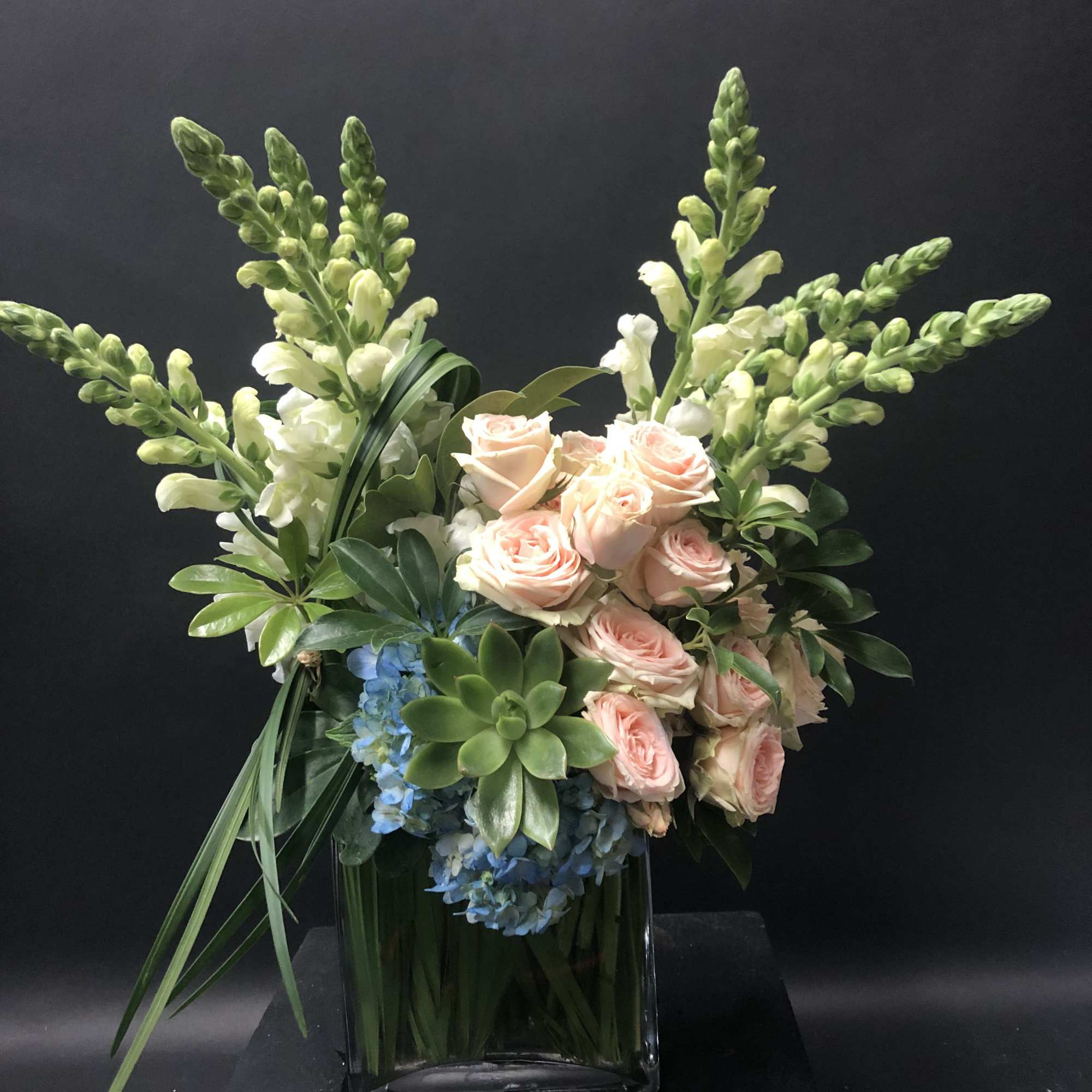 Pink roses and white snapdragons in a square glass vase with blue flowers