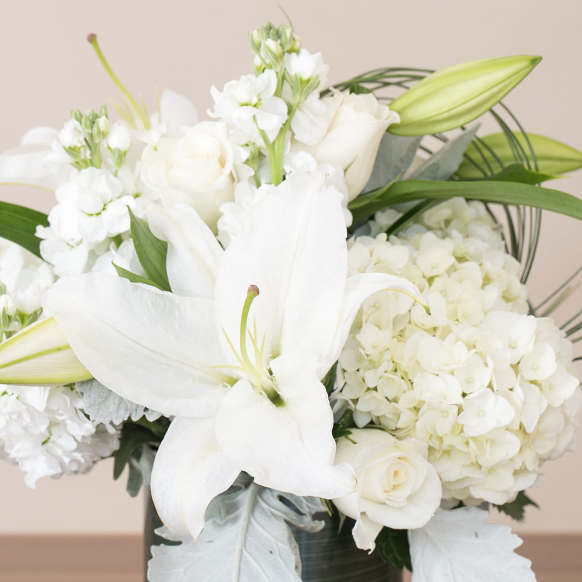 White lilies, roses, hydrangeas, and stock arranged in a compact vase
