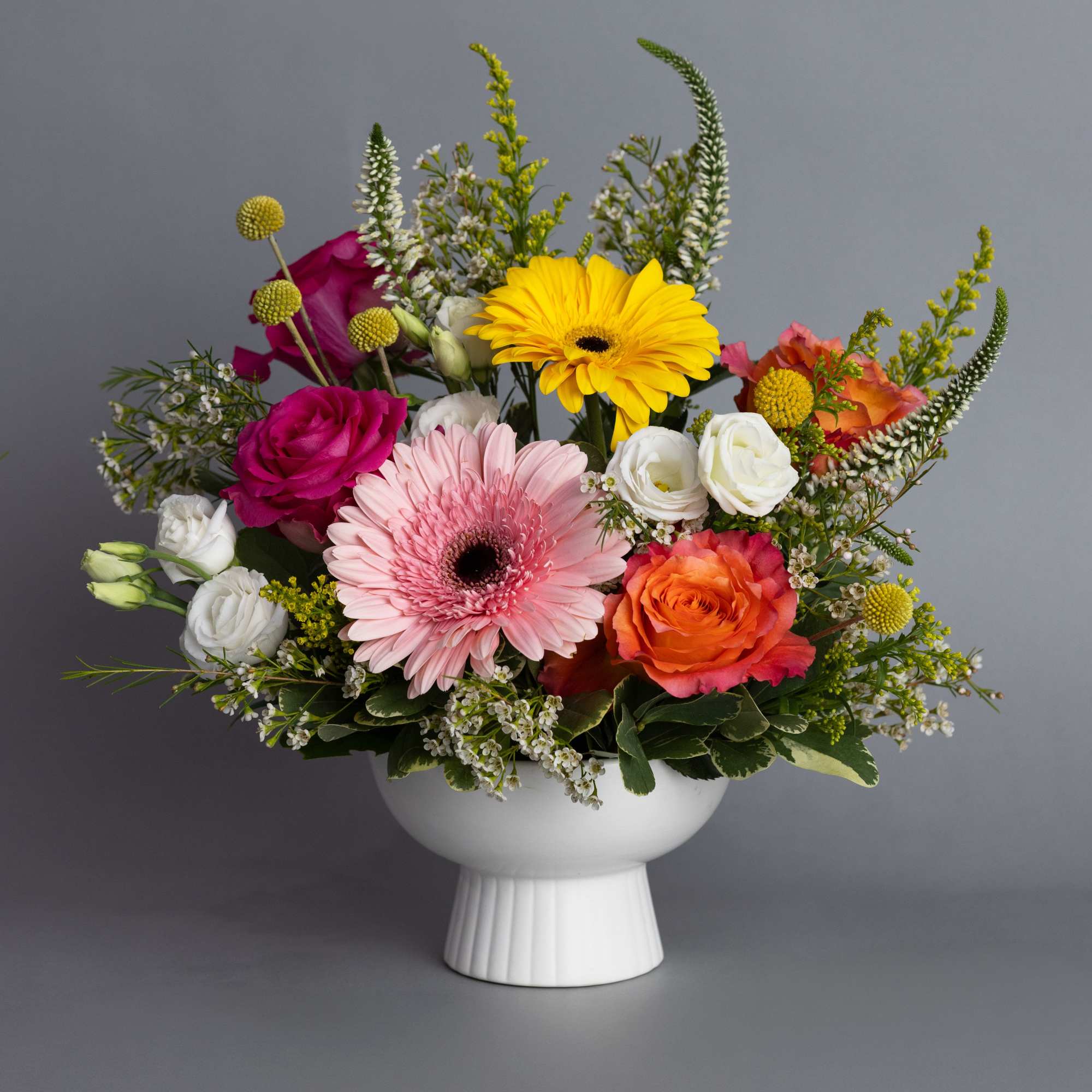 Colorful mix of gerbera daisies, roses, and lisianthus in a white pedestal bowl