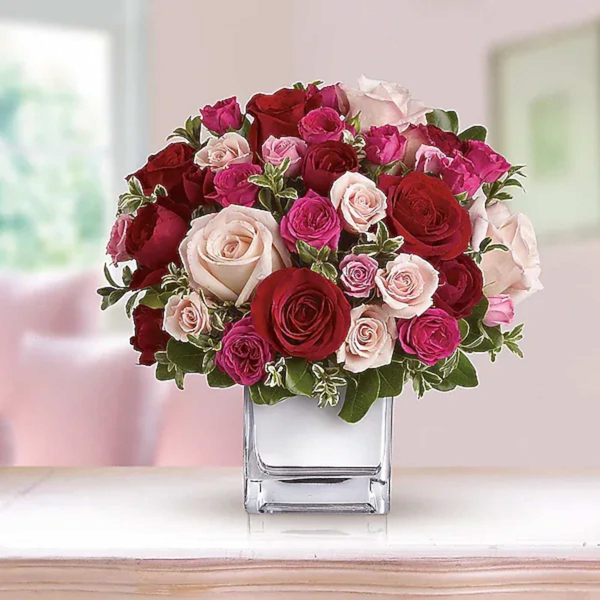 Bouquet of red, pink, and blush roses in a clear square vase