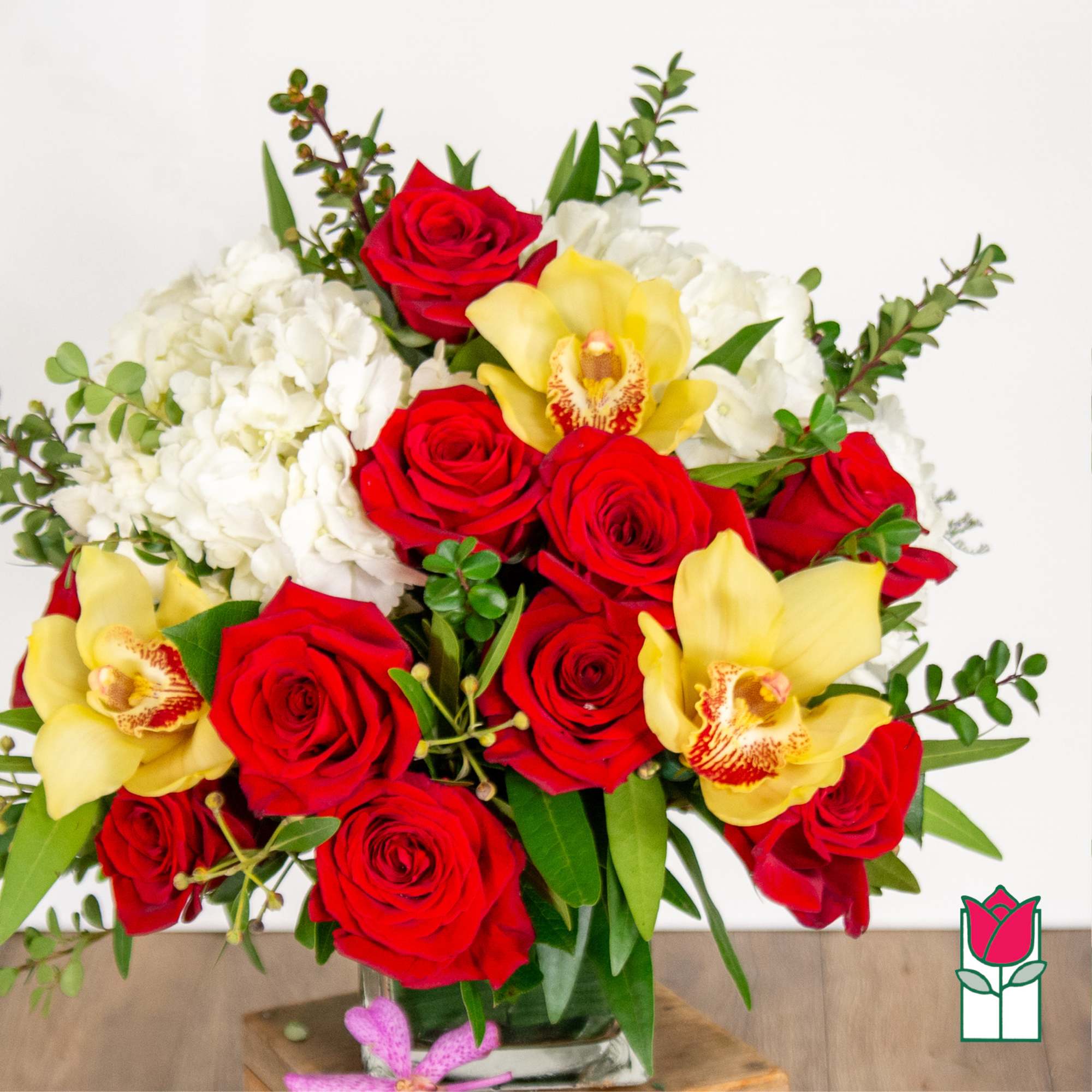 Bouquet of red roses, white hydrangeas, and yellow orchids in a glass vase