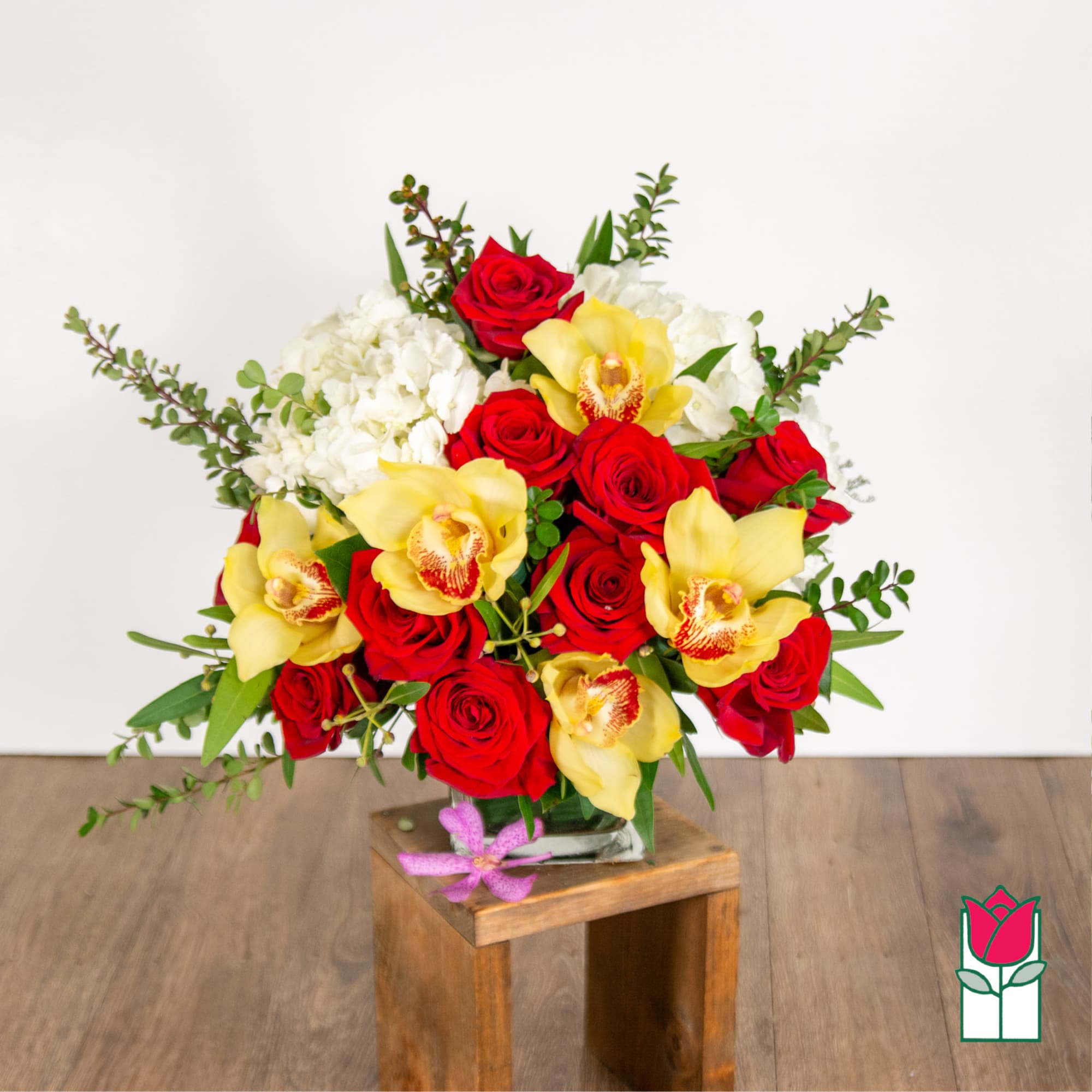 Bouquet of red roses, yellow orchids, and white flowers in a glass vase
