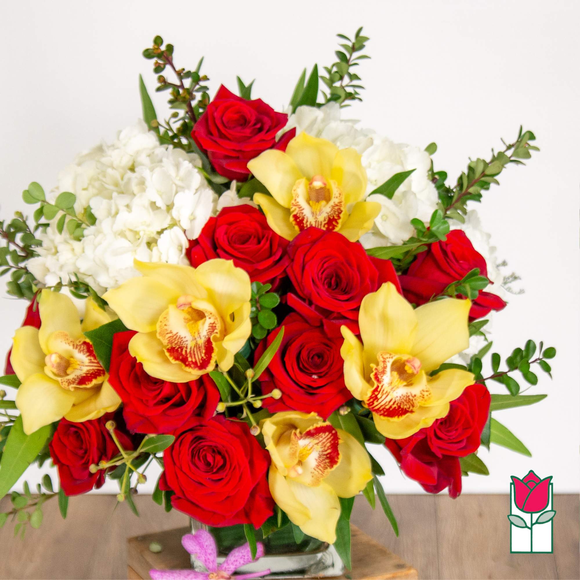 Bouquet of red roses, yellow orchids, and white flowers in a glass vase