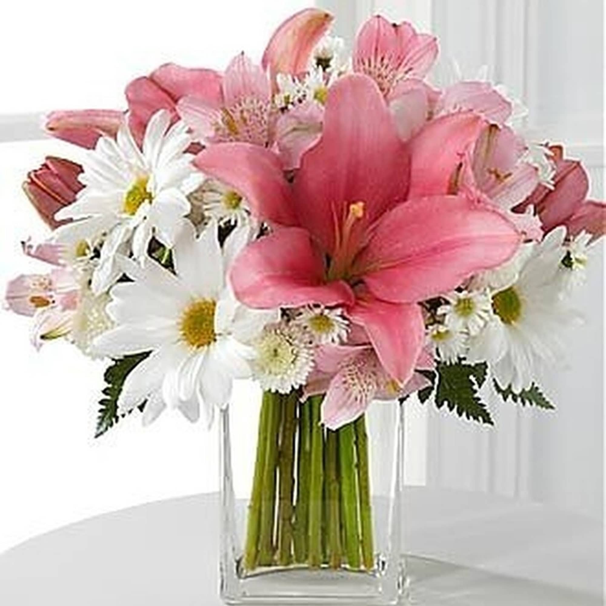 Pink lilies and white daisies arranged in a clear rectangular glass vase