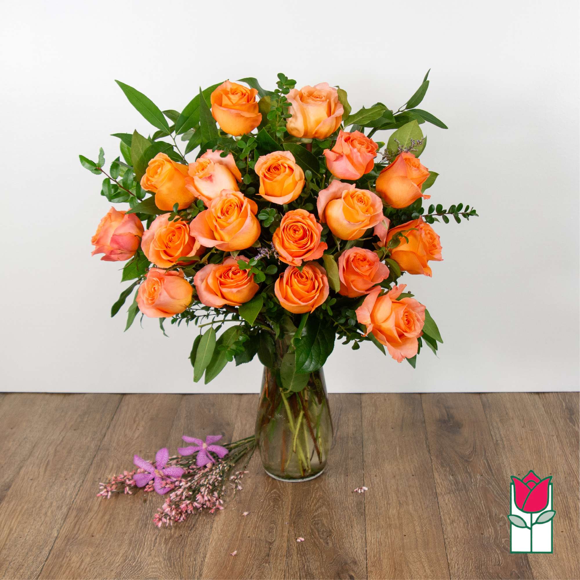 Orange roses arranged in a clear glass vase with greenery.
