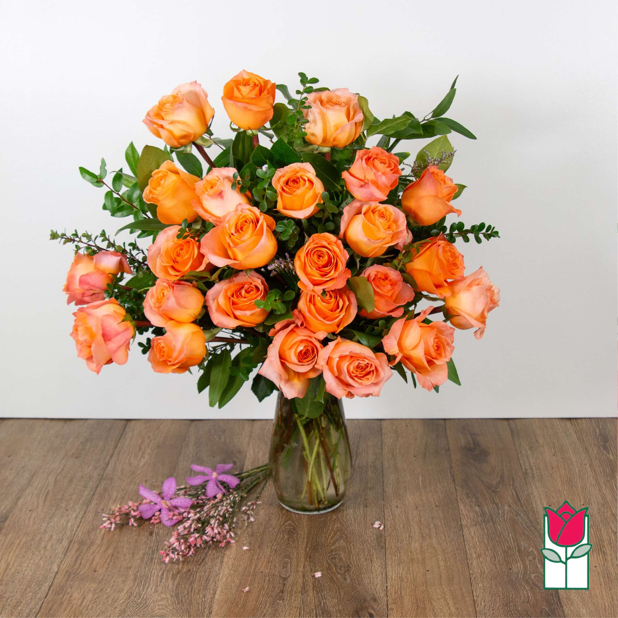 Orange roses arranged in a clear glass vase with greenery