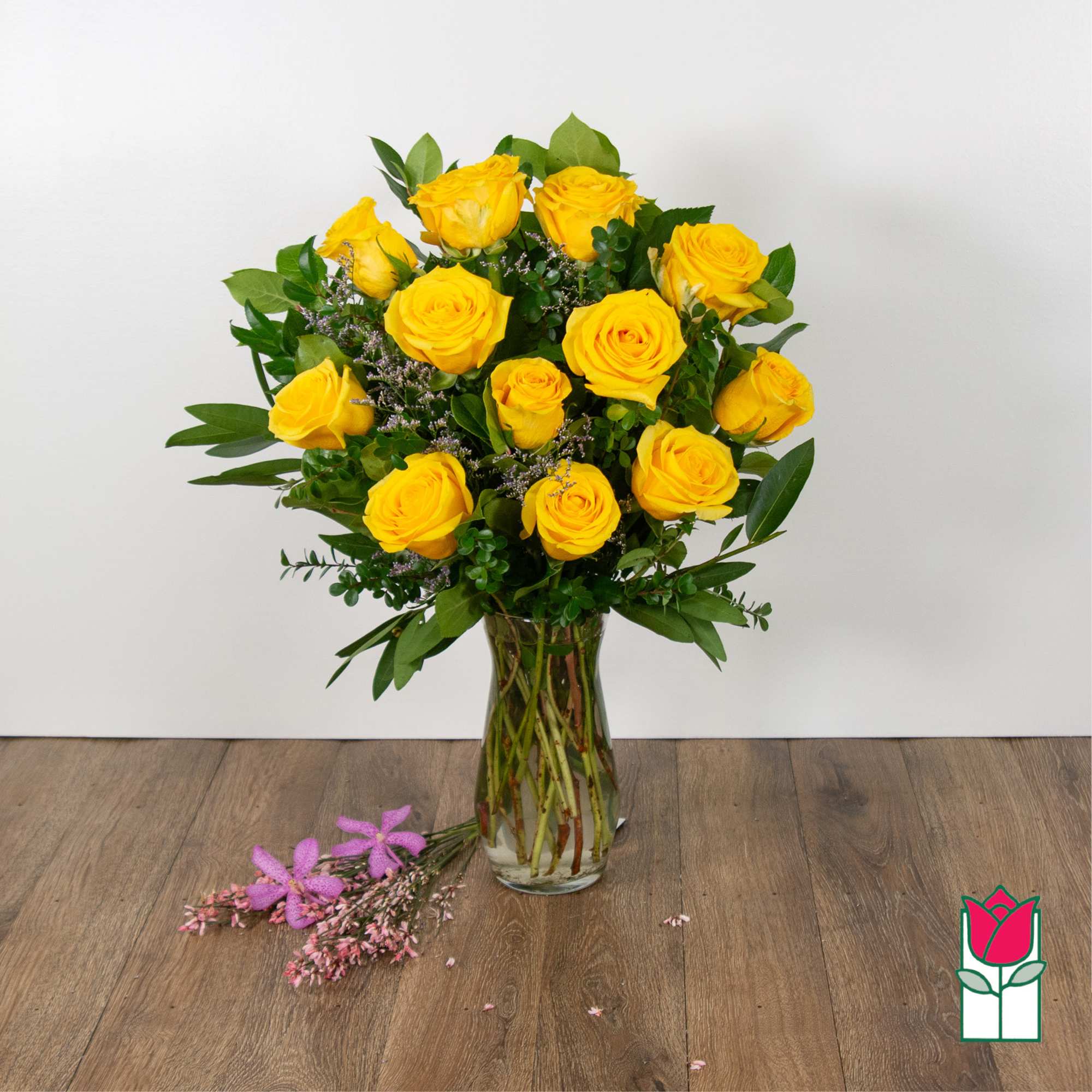 Yellow roses arranged in a clear glass vase with greenery