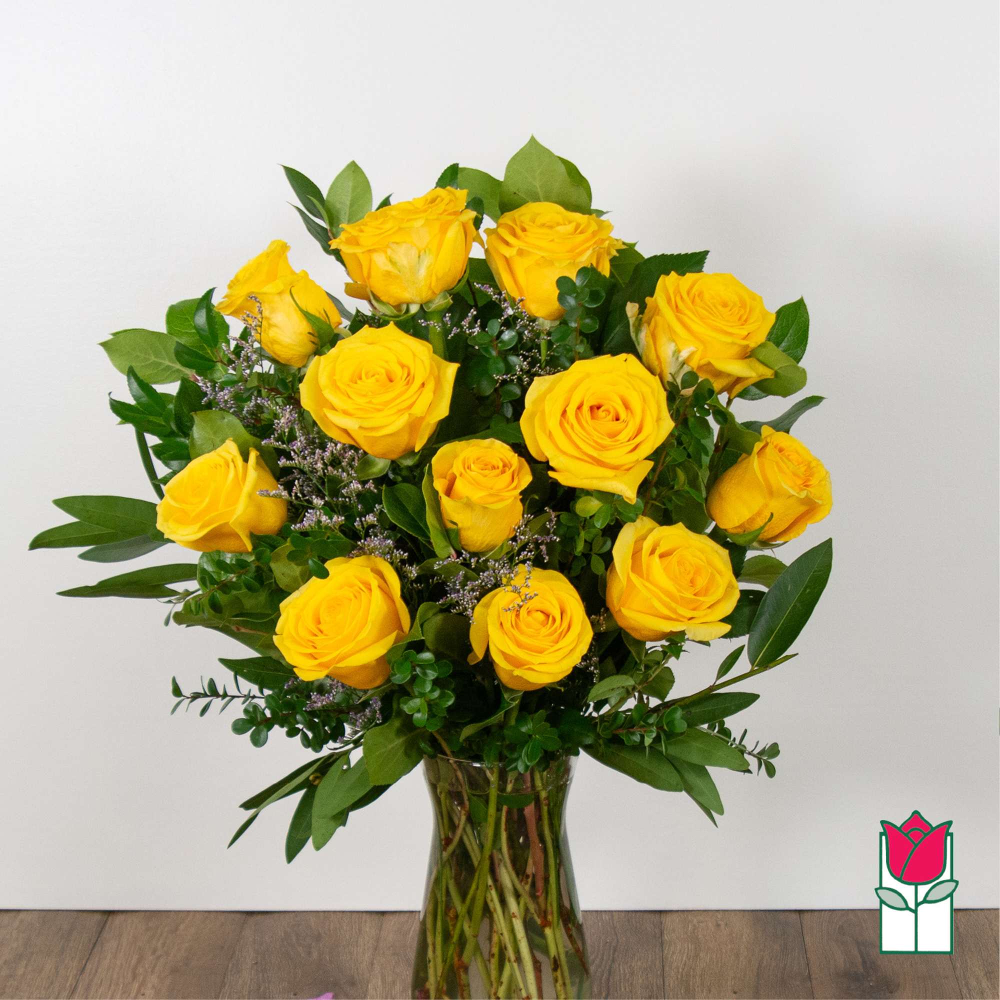 Yellow roses arranged in a clear glass vase with greenery