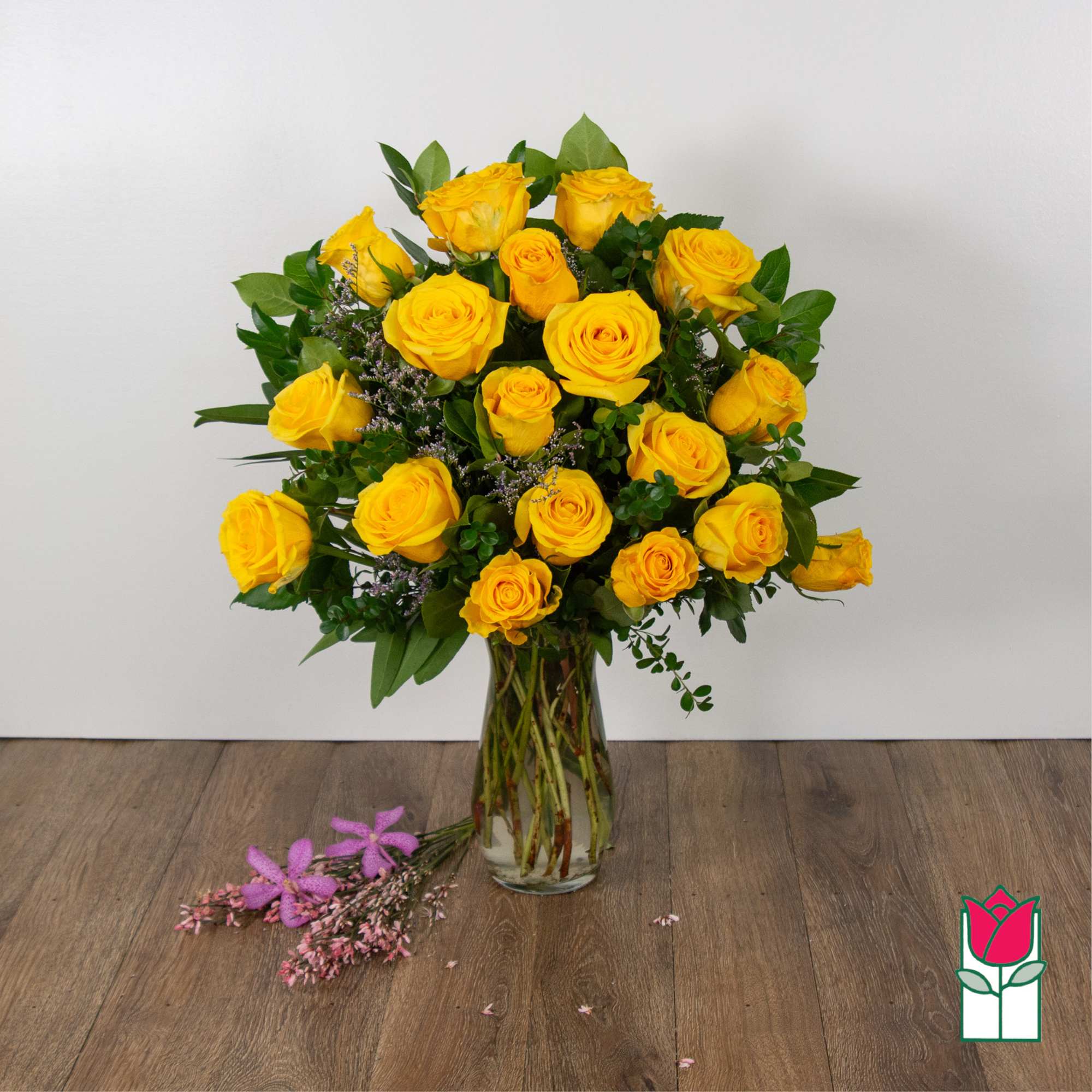 Yellow roses arranged in a clear glass vase with greenery