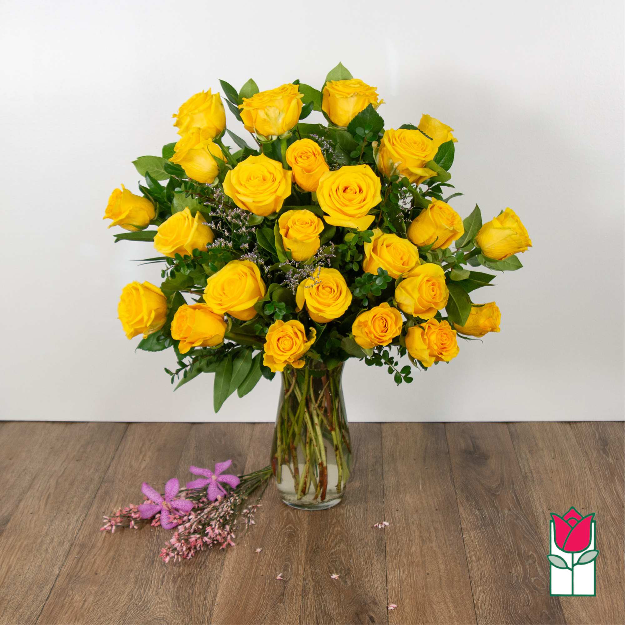Yellow roses arranged in a clear glass vase with greenery