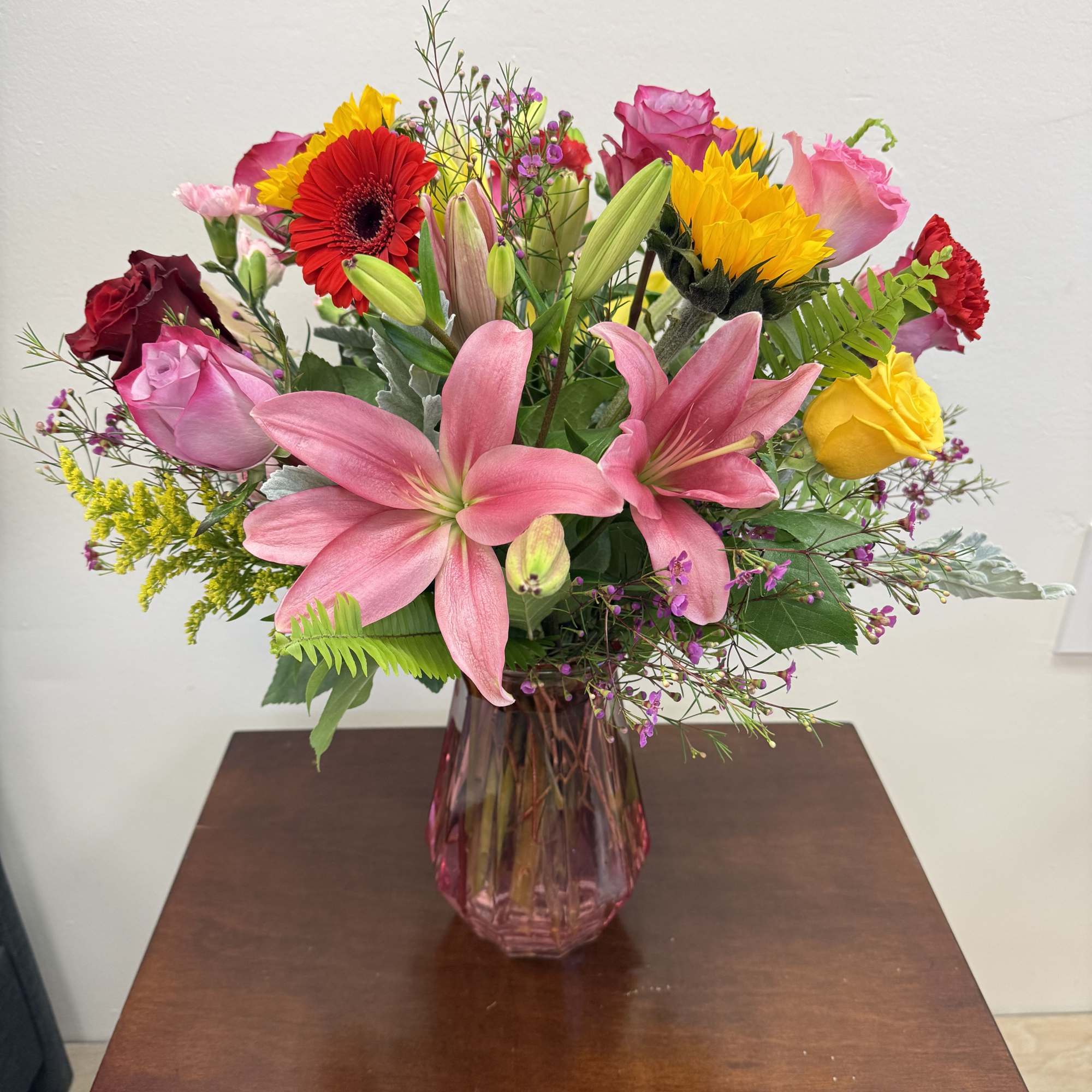 Mixed bouquet of pink lilies, roses, and bright gerbera daisies in a pink glass vase