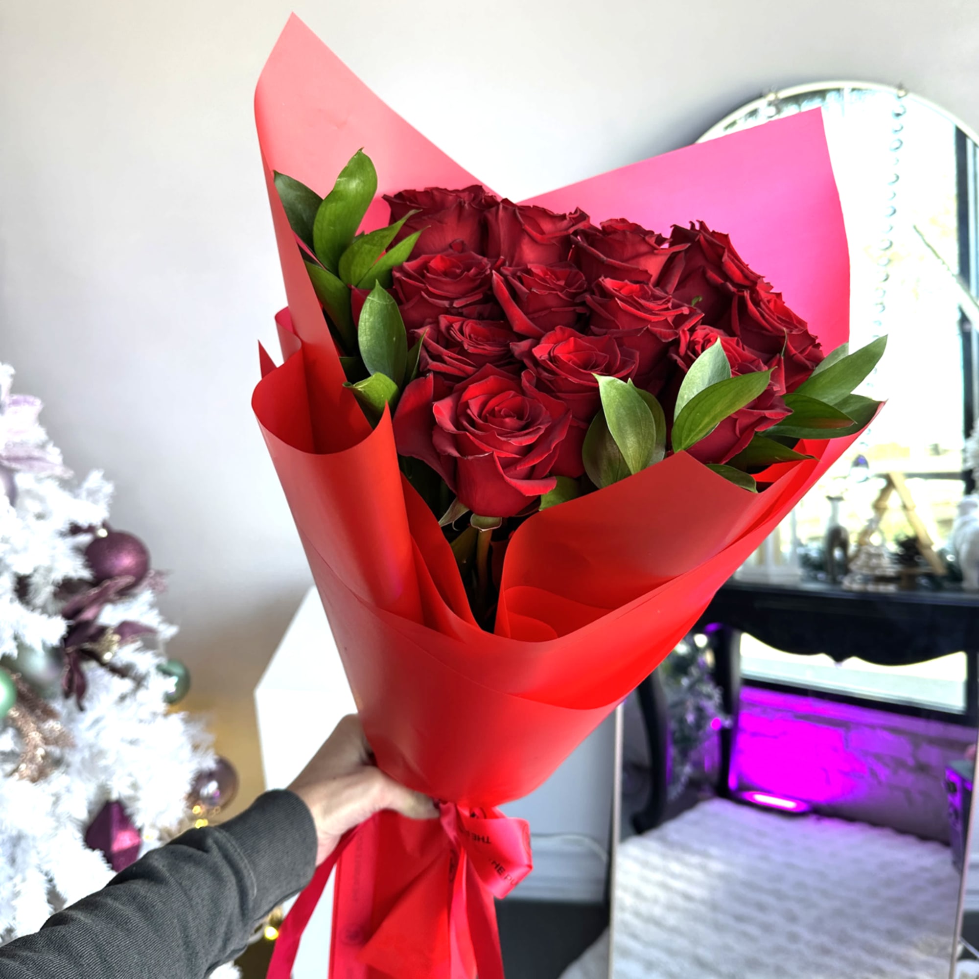 Hand-held bouquet of red roses wrapped in bright red paper