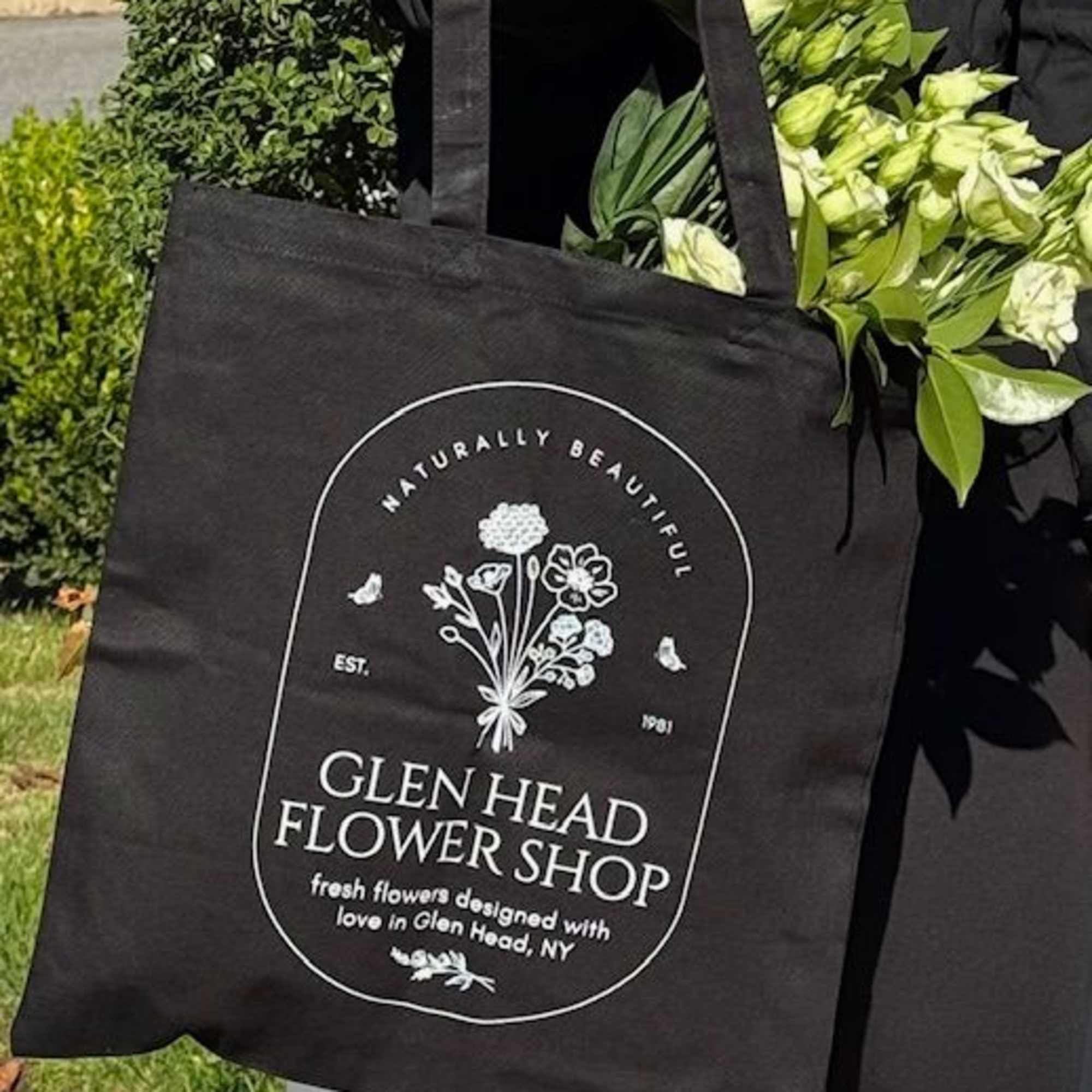Black flower shop tote bag with white logo, holding pale flowers