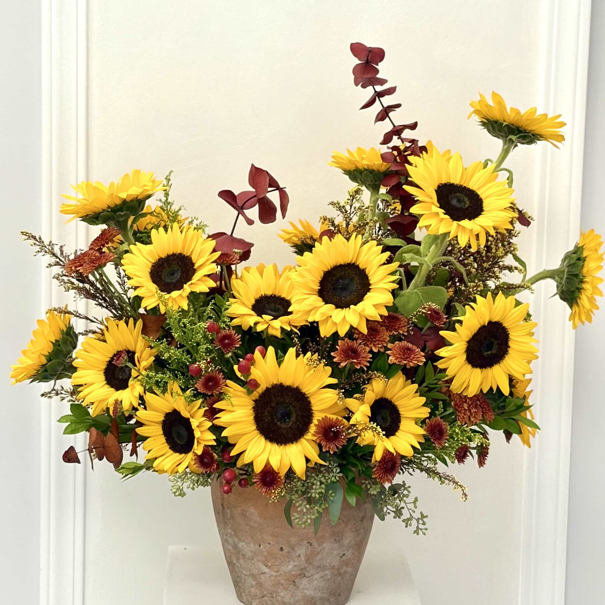 Large arrangement of bright yellow sunflowers with red accents in a rustic clay pot