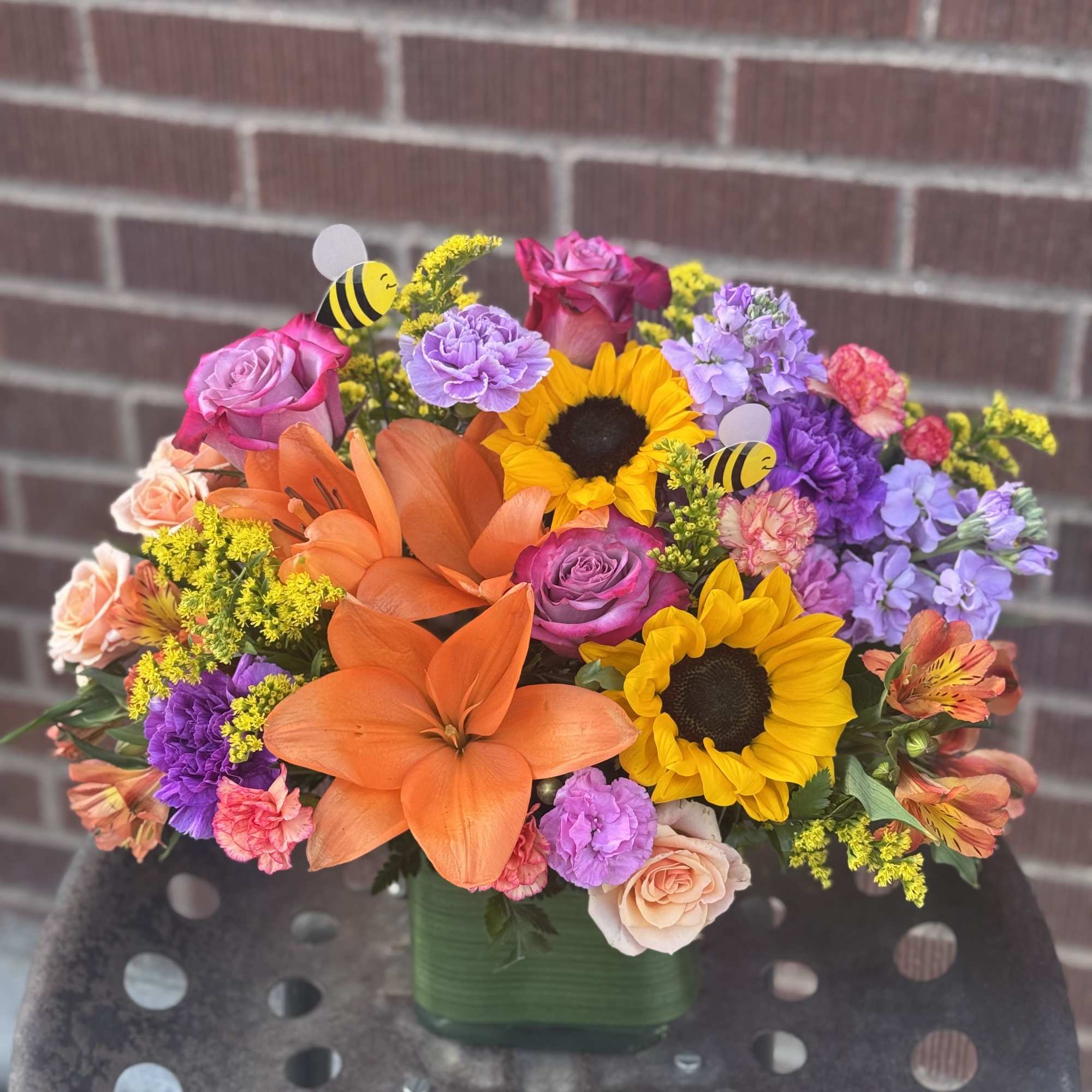 Colorful mixed bouquet in a green vase with sunflowers, roses, and lilies
