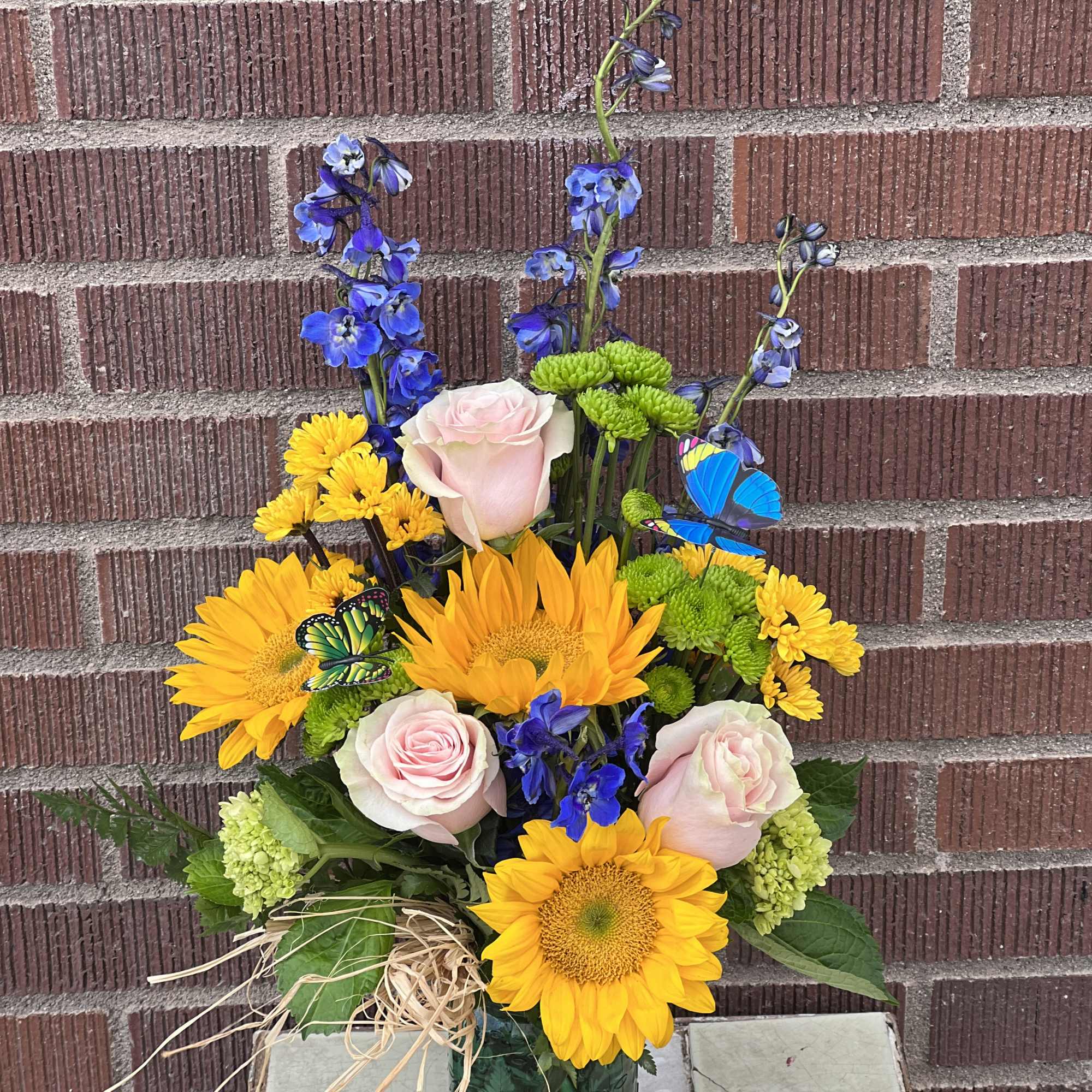 Bouquet of sunflowers, pink roses, and blue flowers in a green vase