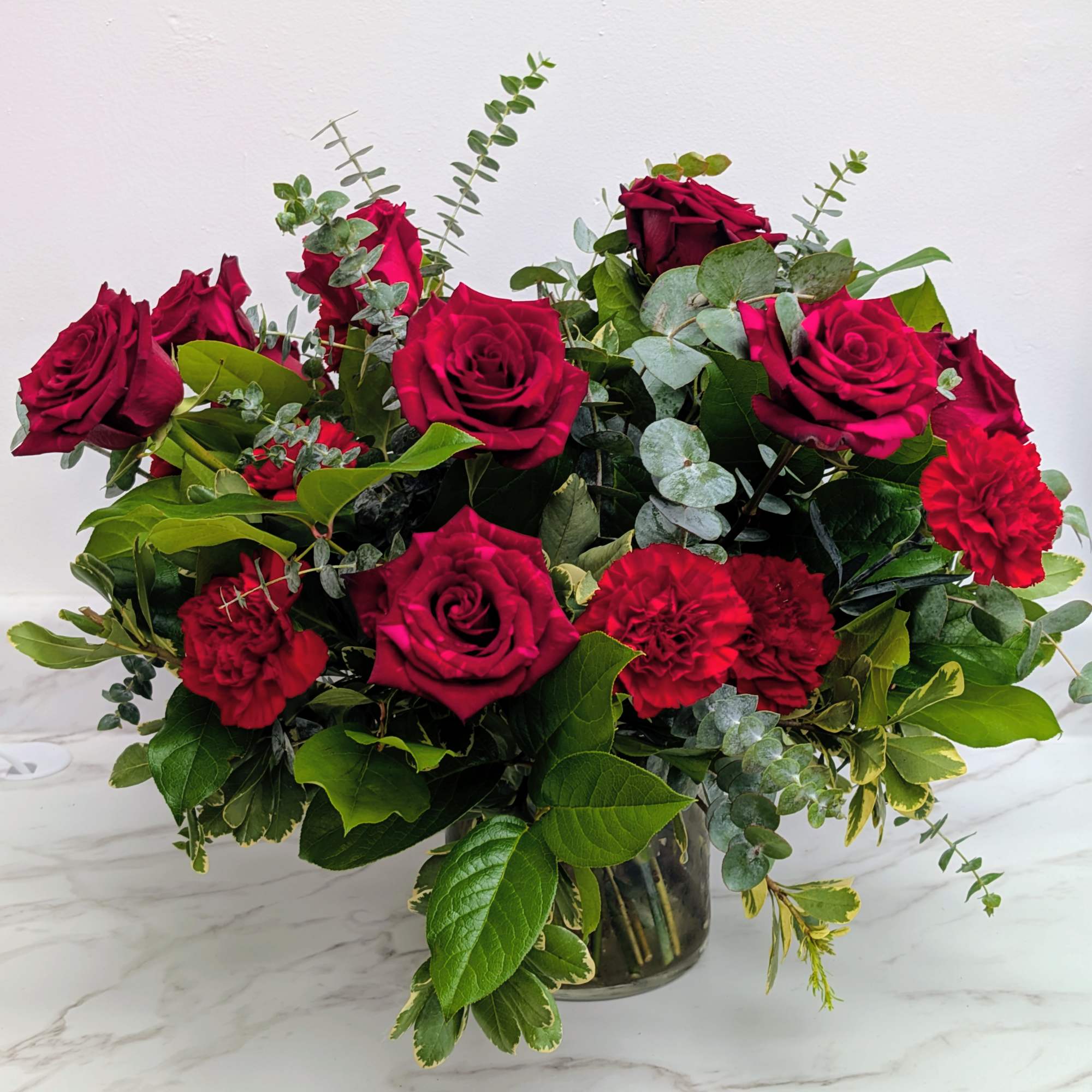 Red roses and carnations in a glass vase with mixed greenery