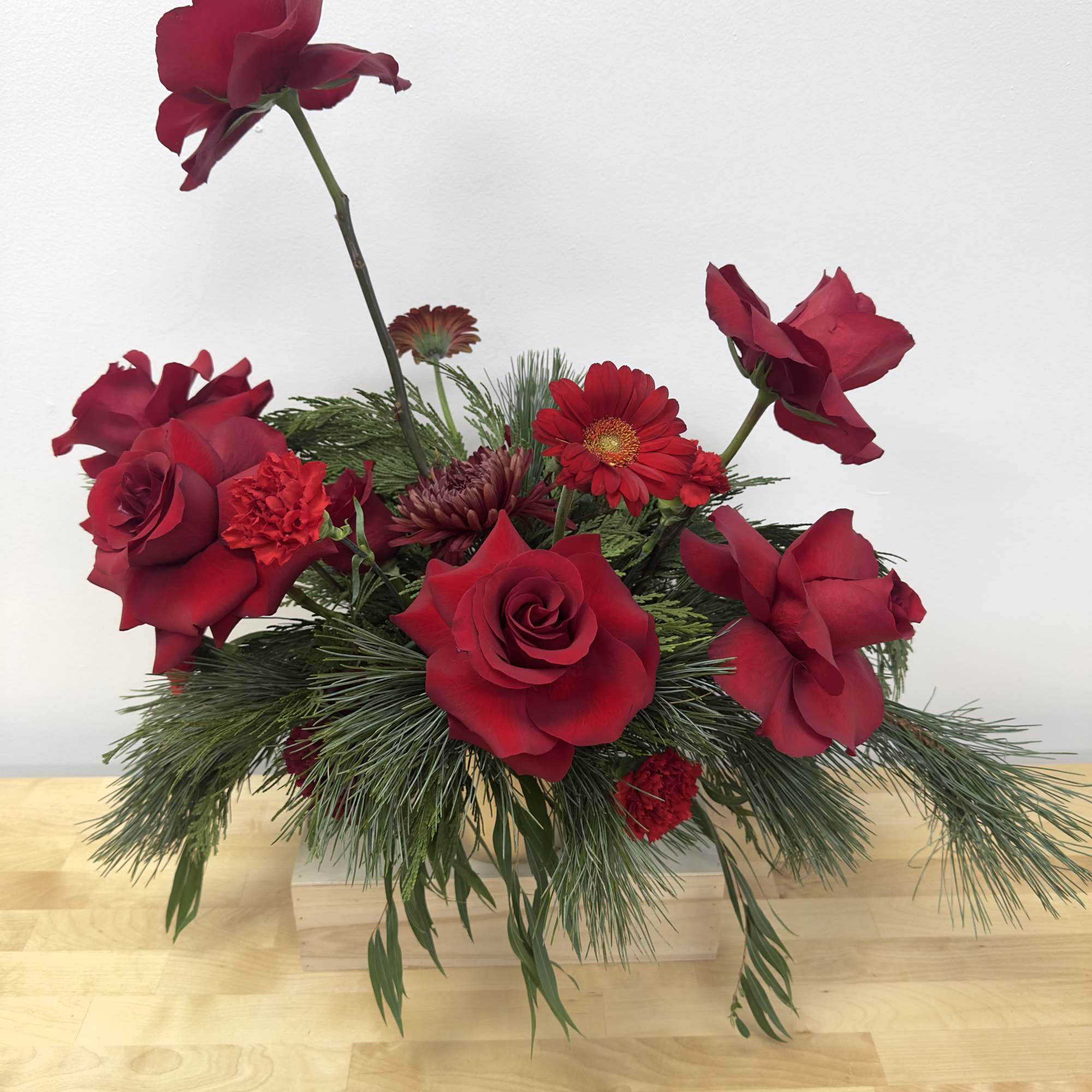 Red roses and mixed red flowers in a low arrangement with pine greenery