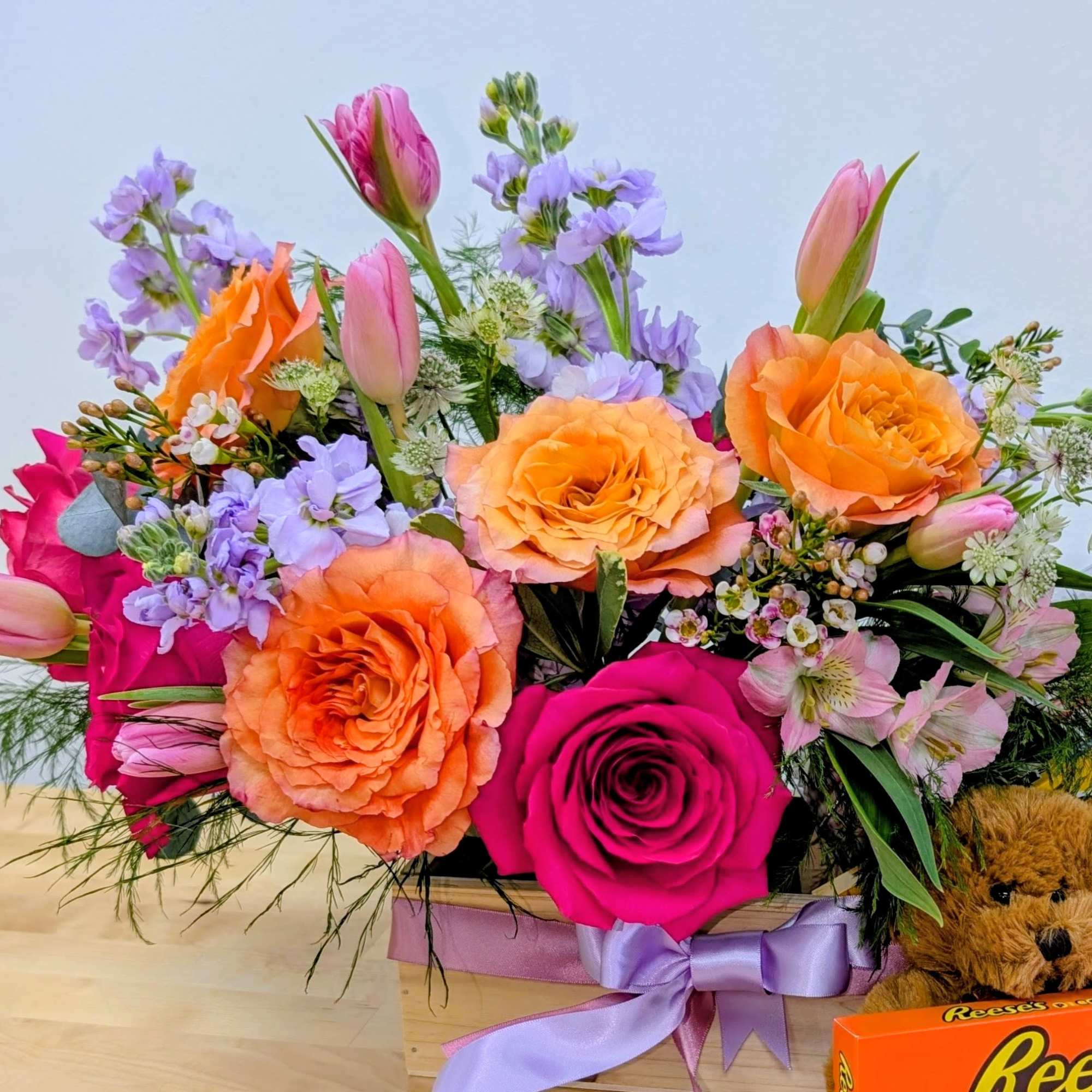 Mixed bouquet with orange and pink roses, tulips, and lavender flowers in a wooden box