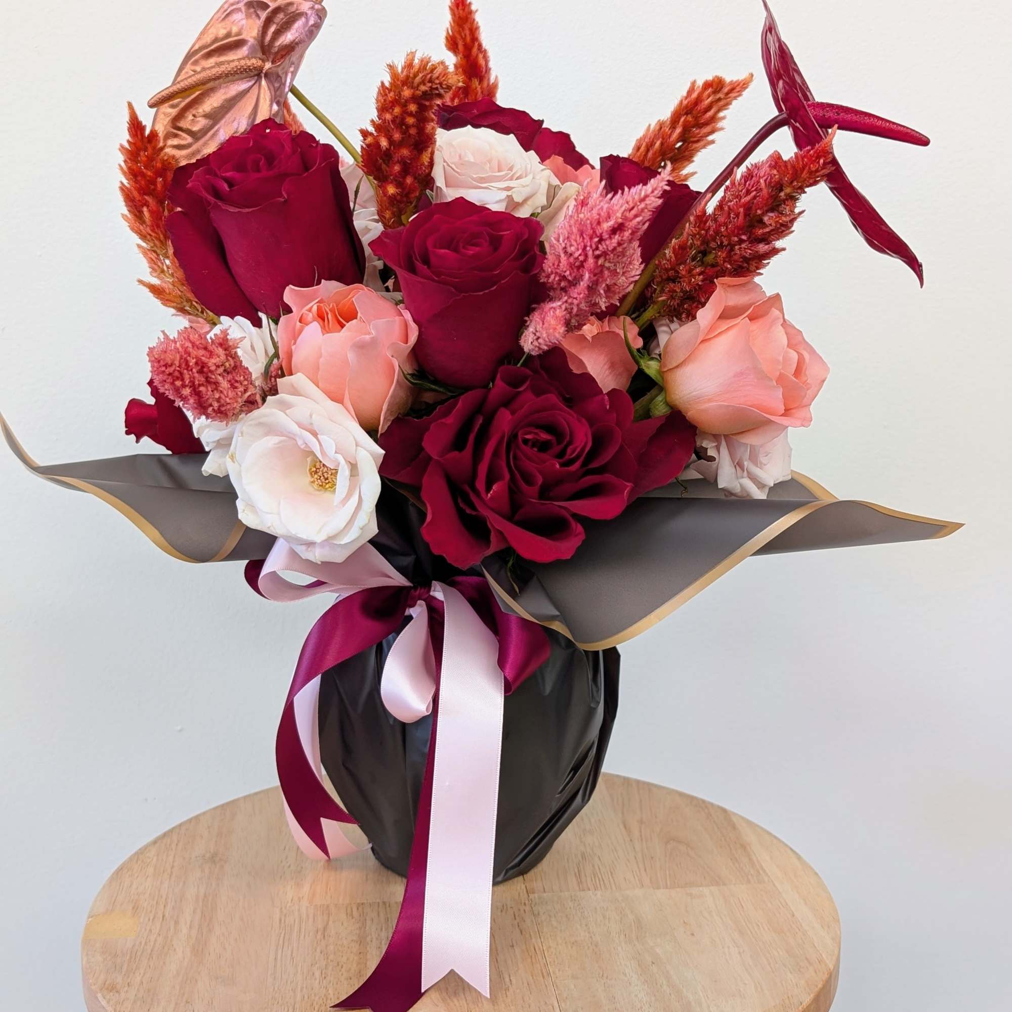 Bouquet of red, blush, and white roses in black wrap with ribbon