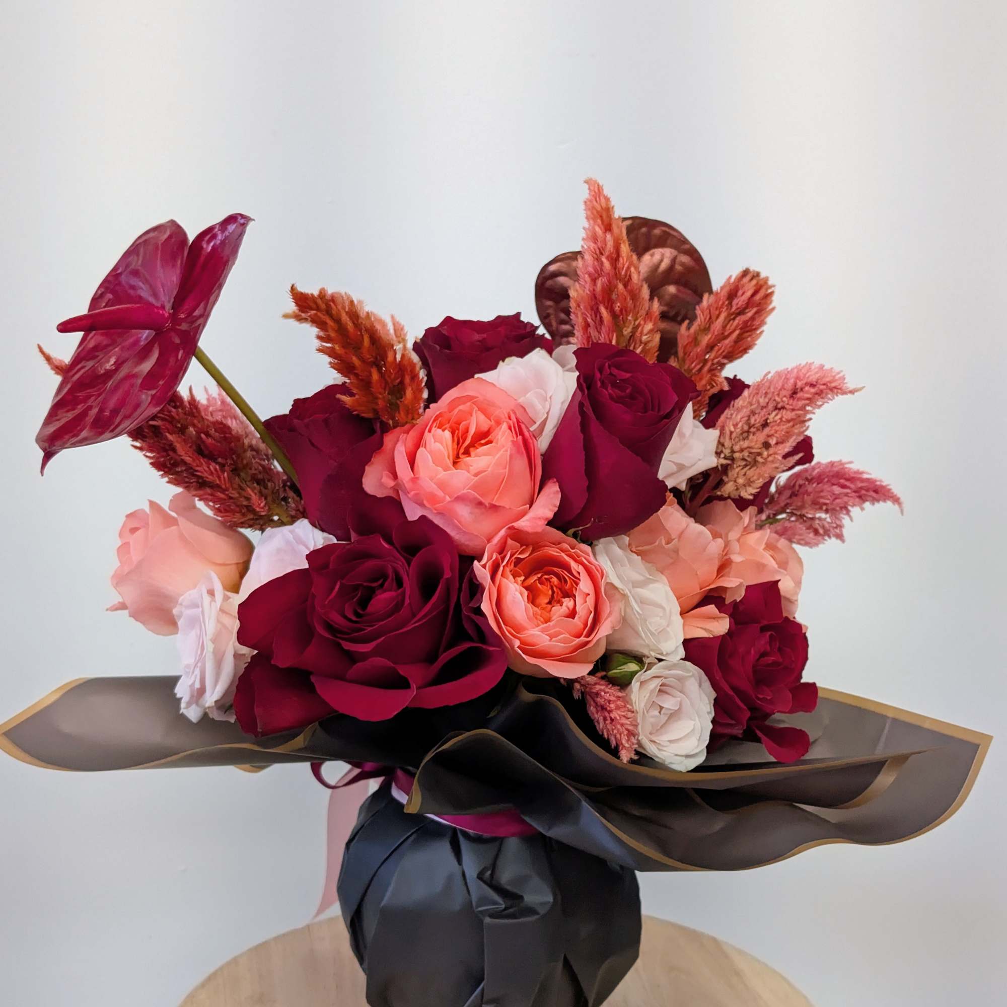 Bouquet of red, pink, and white roses with tropical foliage in black wrap