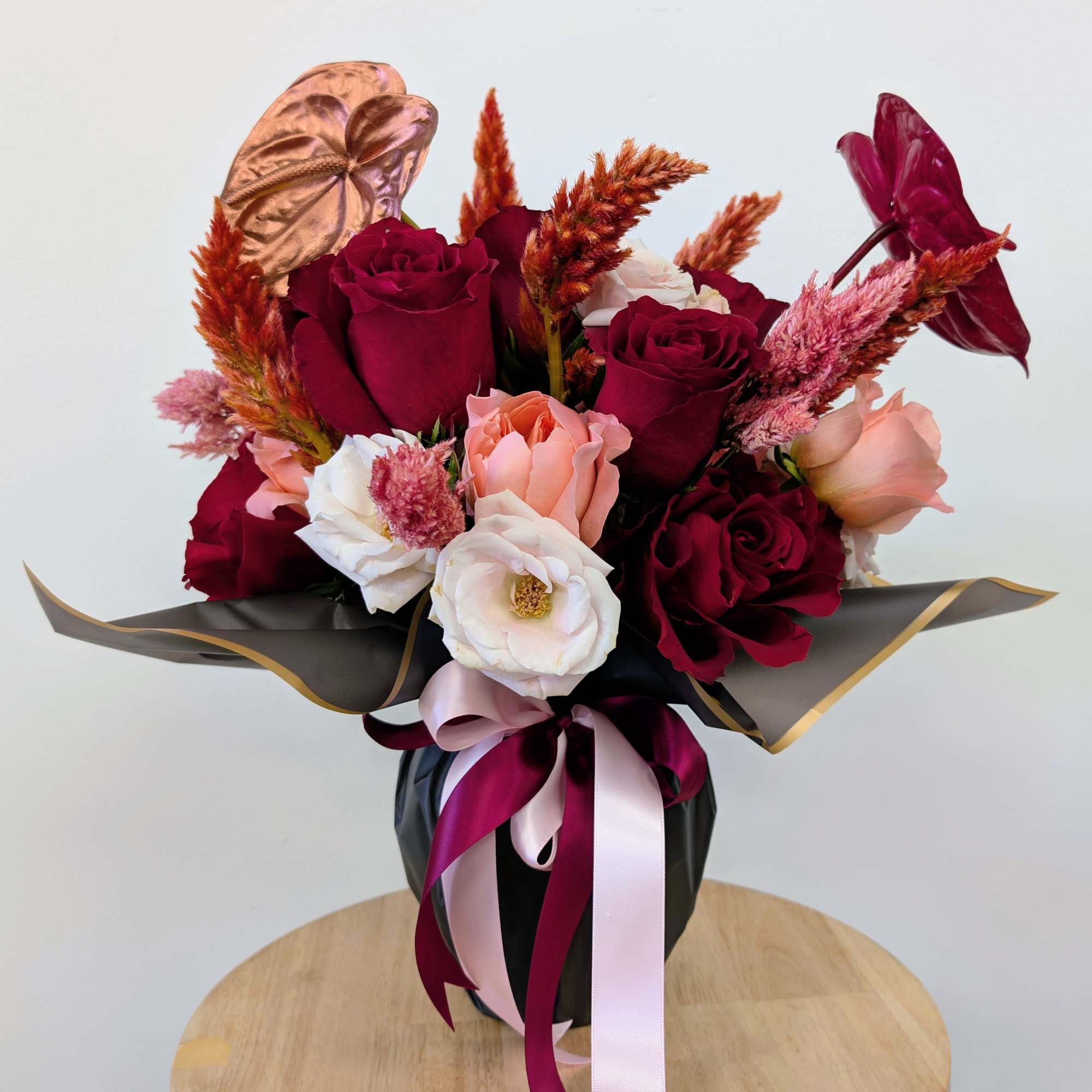 Bouquet of burgundy and blush roses in black wrap with ribbon