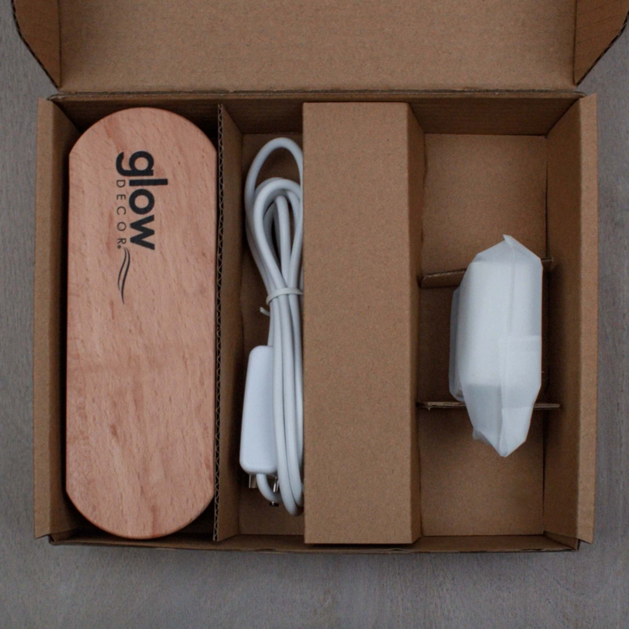 Open cardboard box with a wooden Glow Decor piece, cord, and wrapped accessory