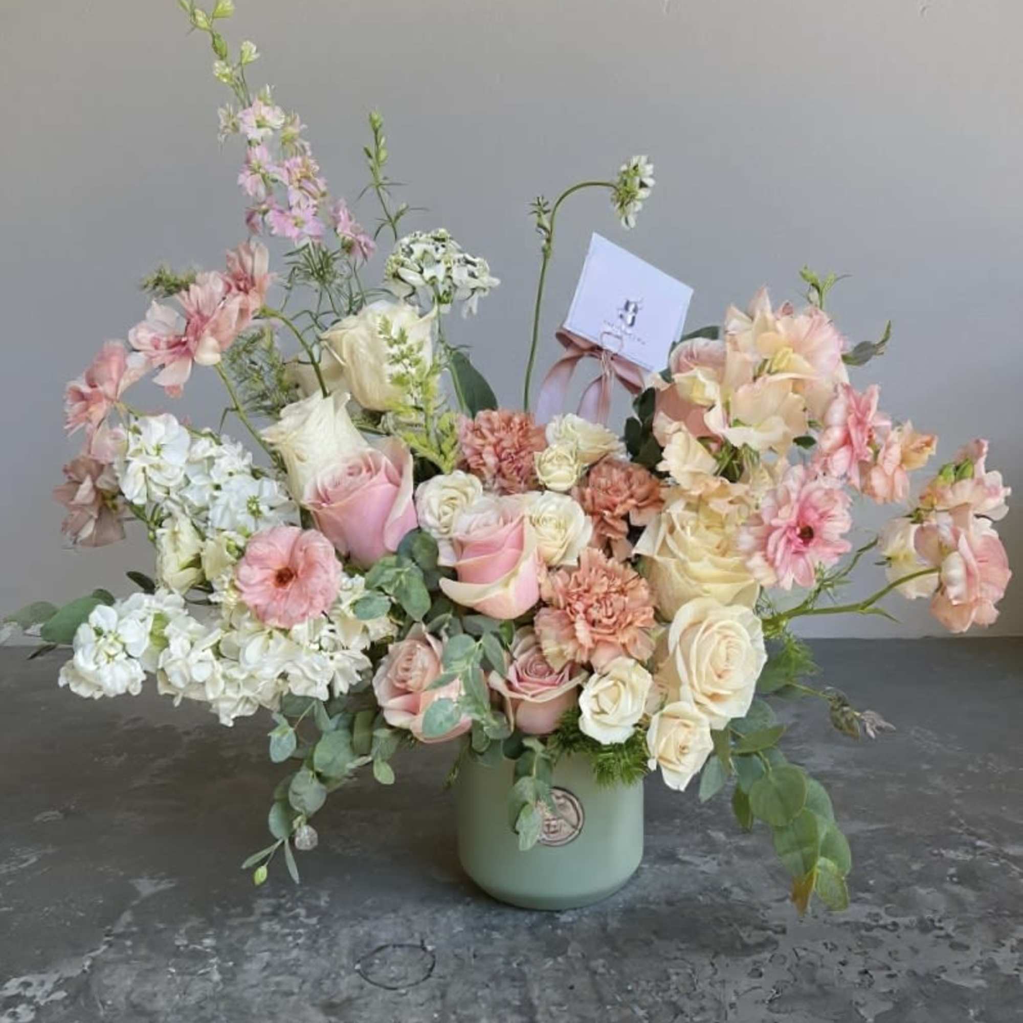 Pastel floral arrangement in a green vase with roses and mixed blooms