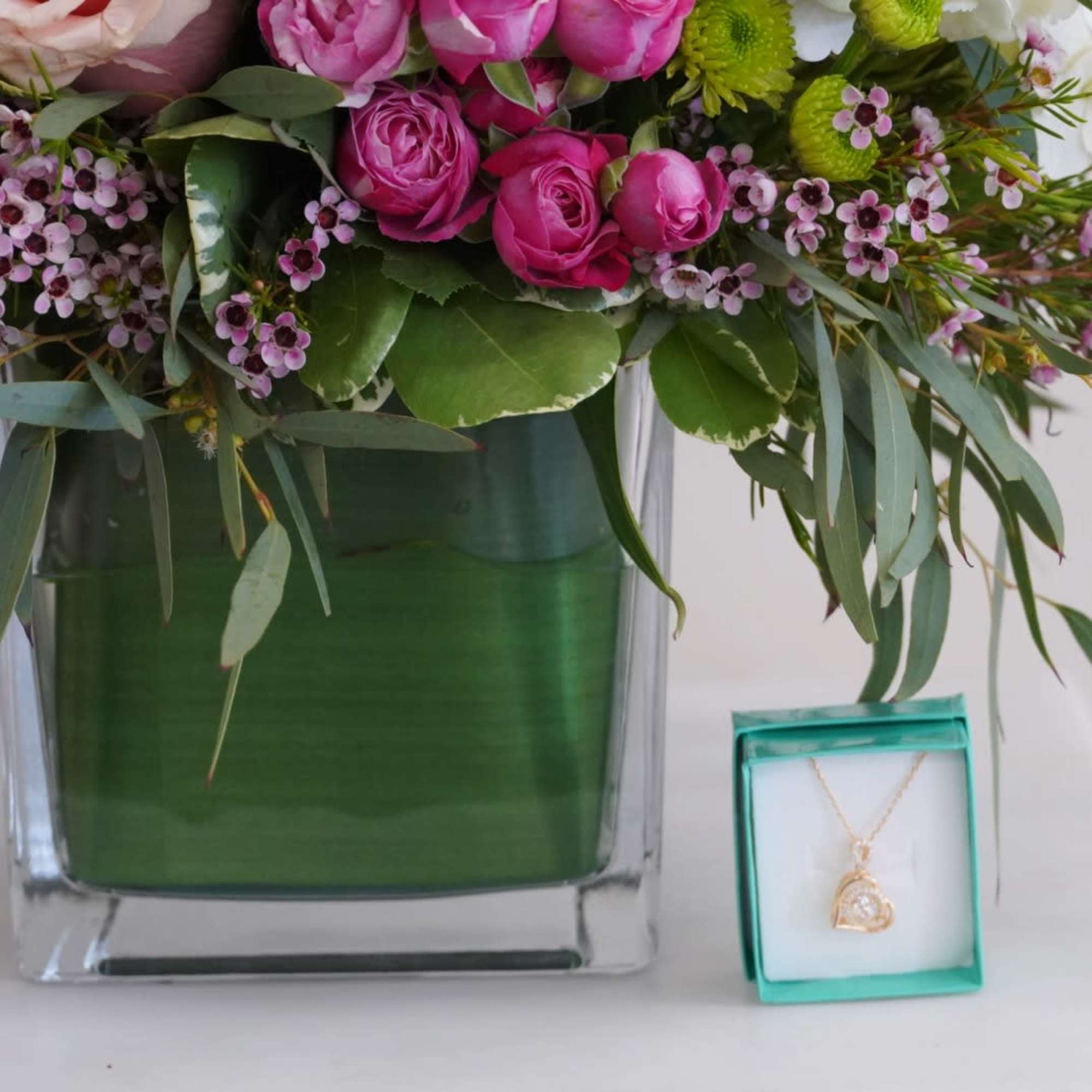 Pink roses in a glass vase beside a necklace gift box