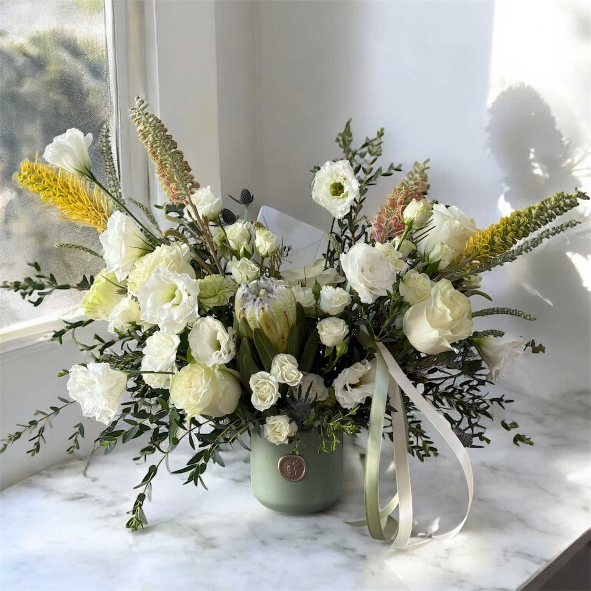 White floral arrangement in a green vase with ribbon