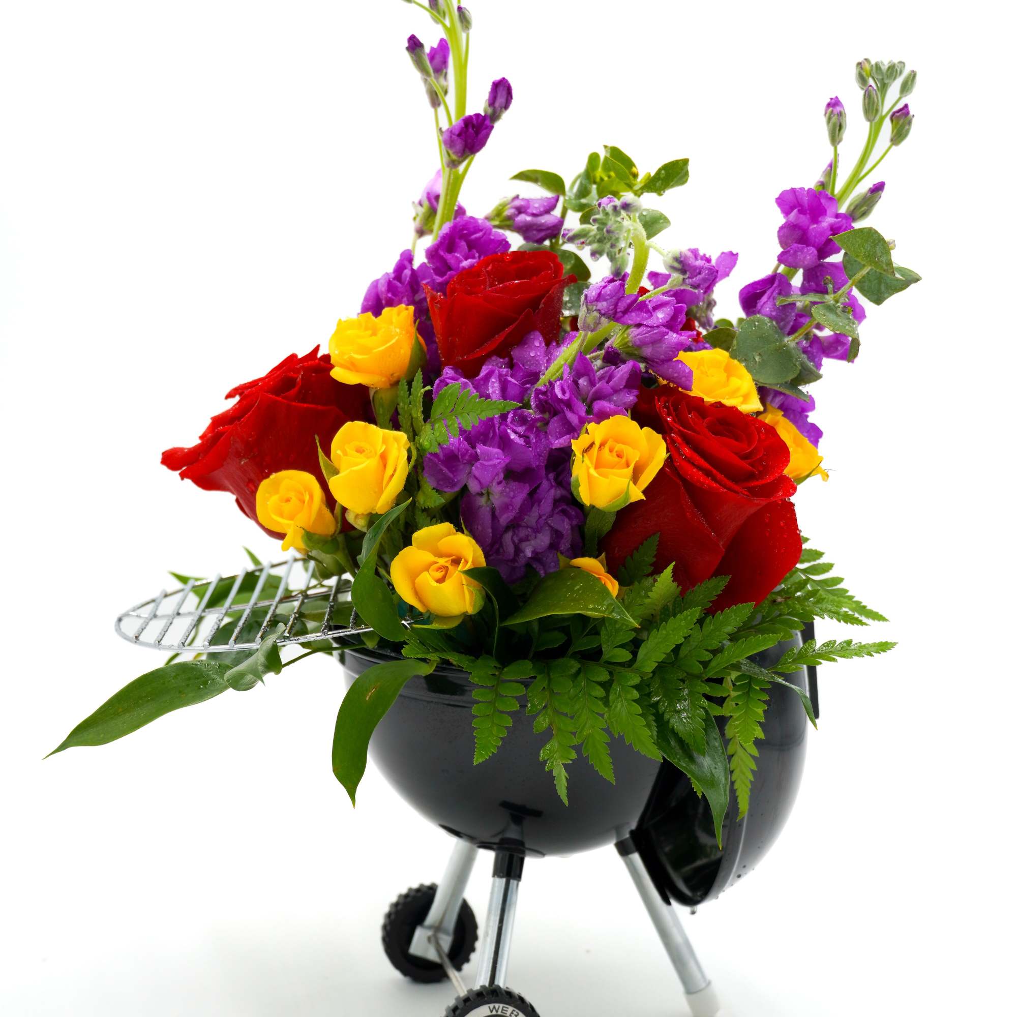 Bouquet of red and yellow roses with purple flowers in a black grill-shaped container