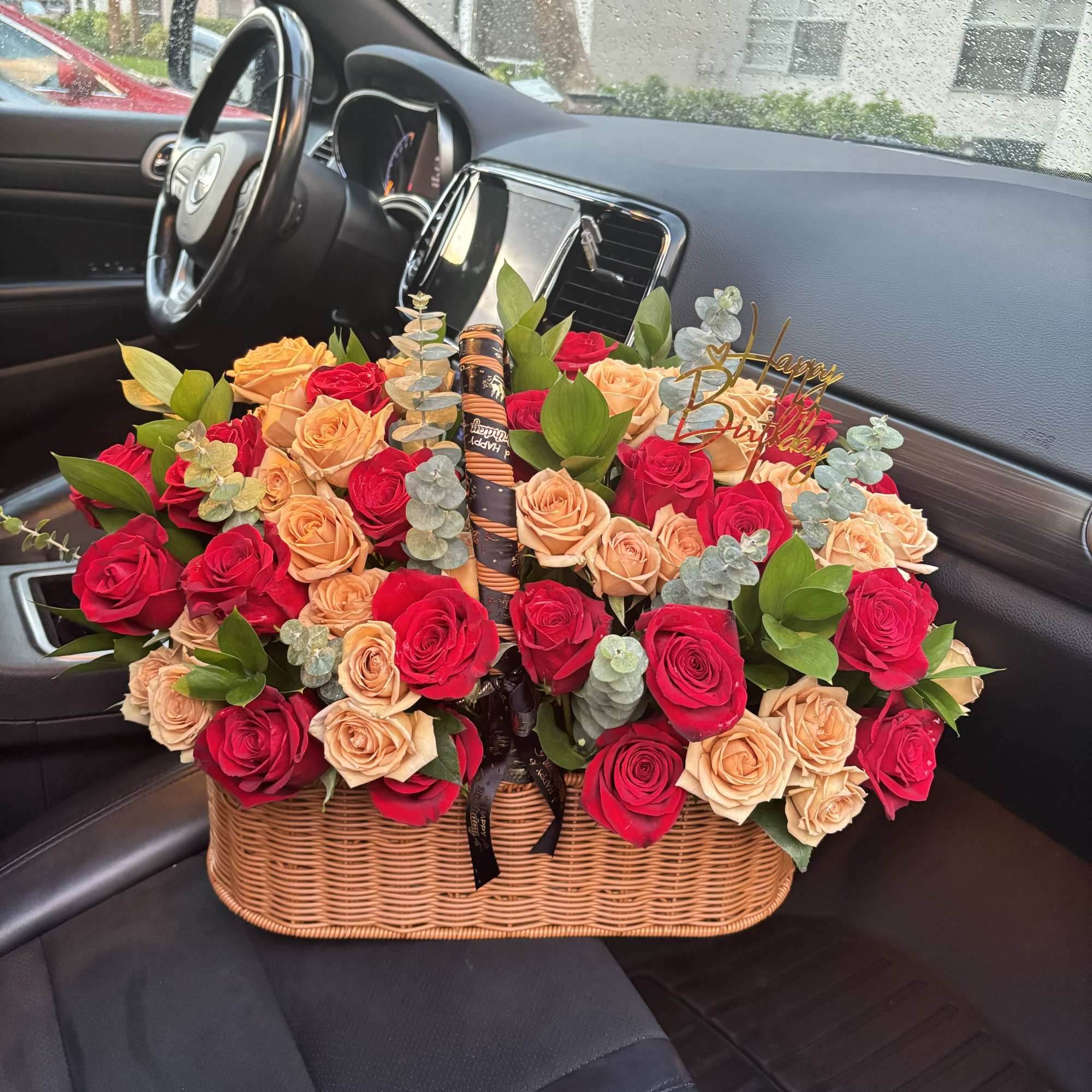 Basket of red and peach roses with a birthday topper in a car seat