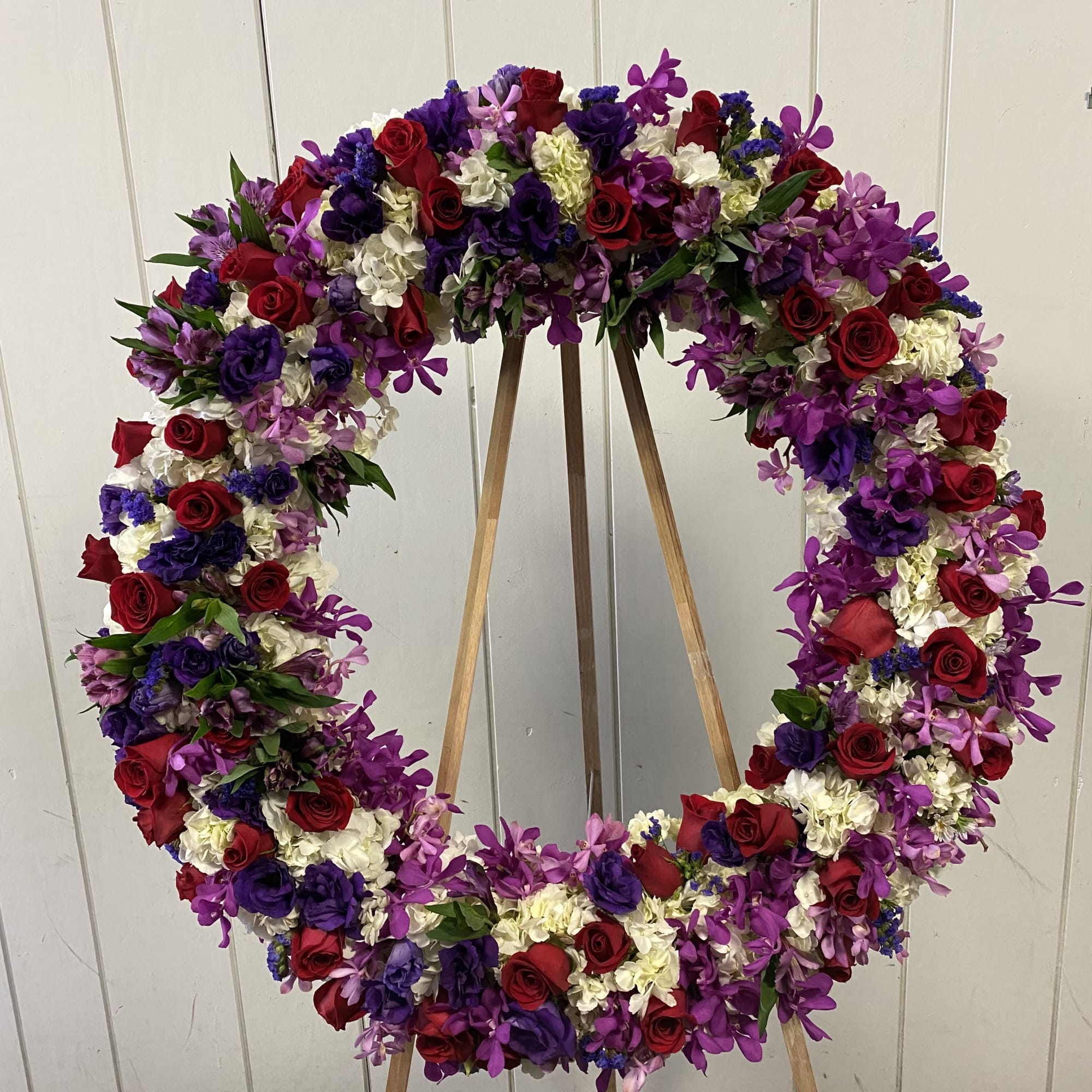 Large floral wreath of red, purple, and white blooms on a wooden easel